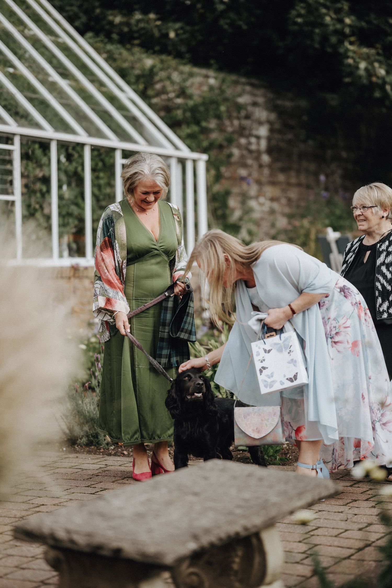 People in colorful attire gathering near a greenhouse in a garden setting.