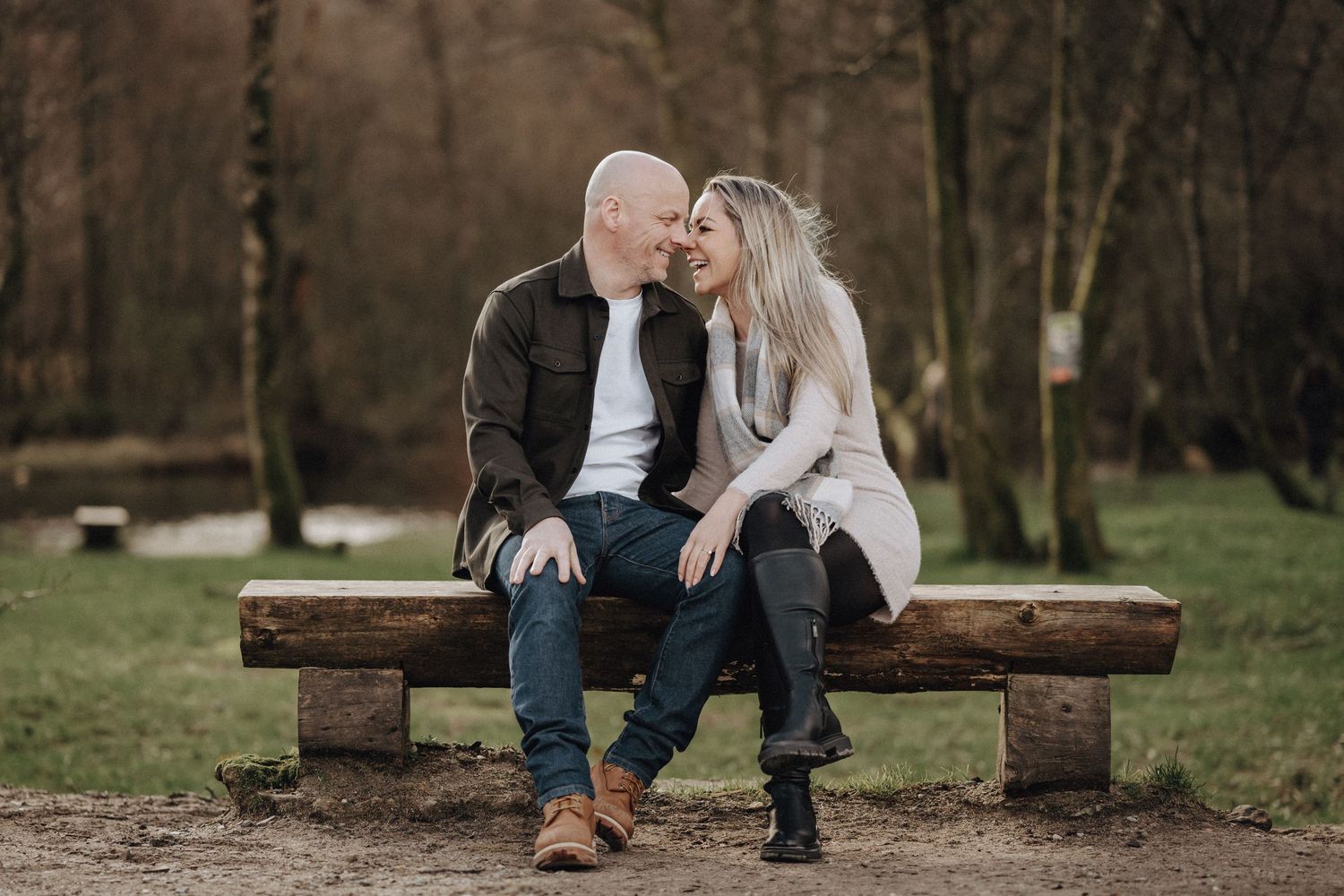 Couple sharing an intimate moment on a wooden bench surrounded by trees.