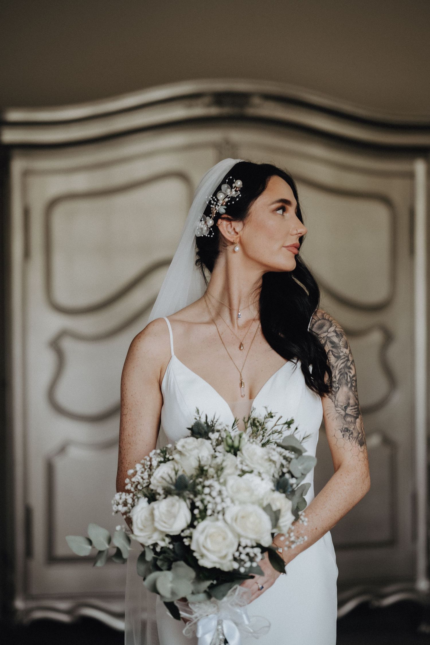 Elegant bride in white slip dress with veil and floral hairpiece holding classic white bouquet.