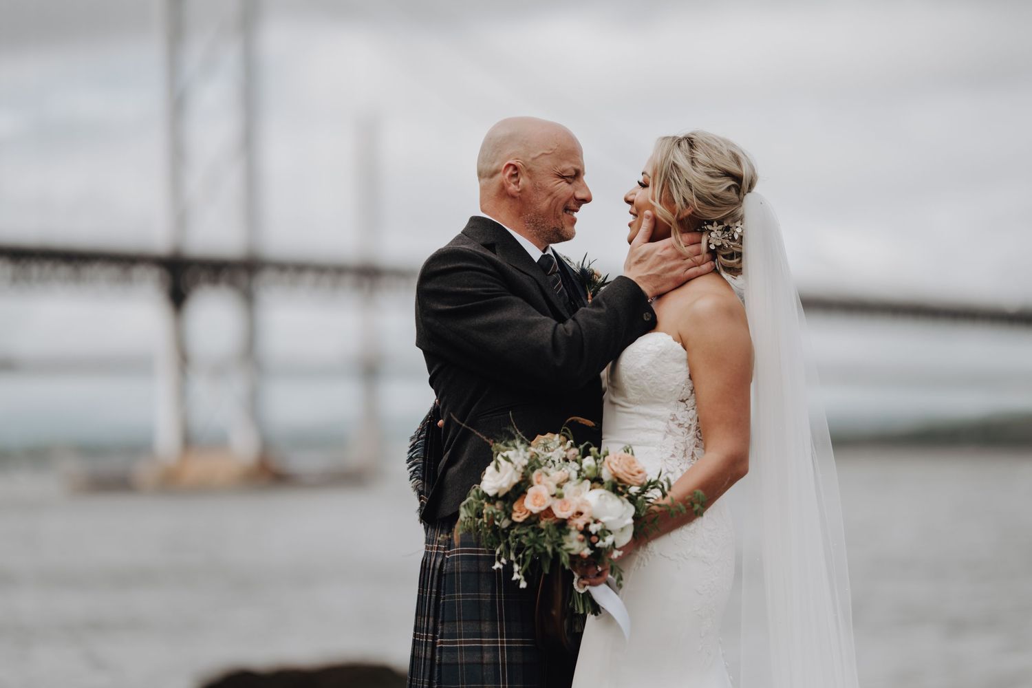 Intimate moment between bride and groom with iconic Scottish bridge in background.