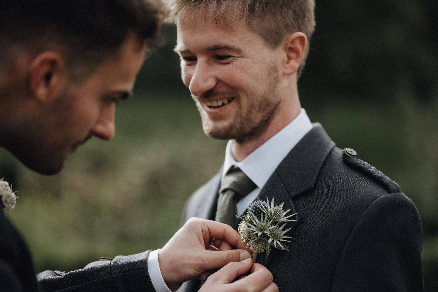 A boutonniere being pinned to a formal suit jacket in an outdoor setting.