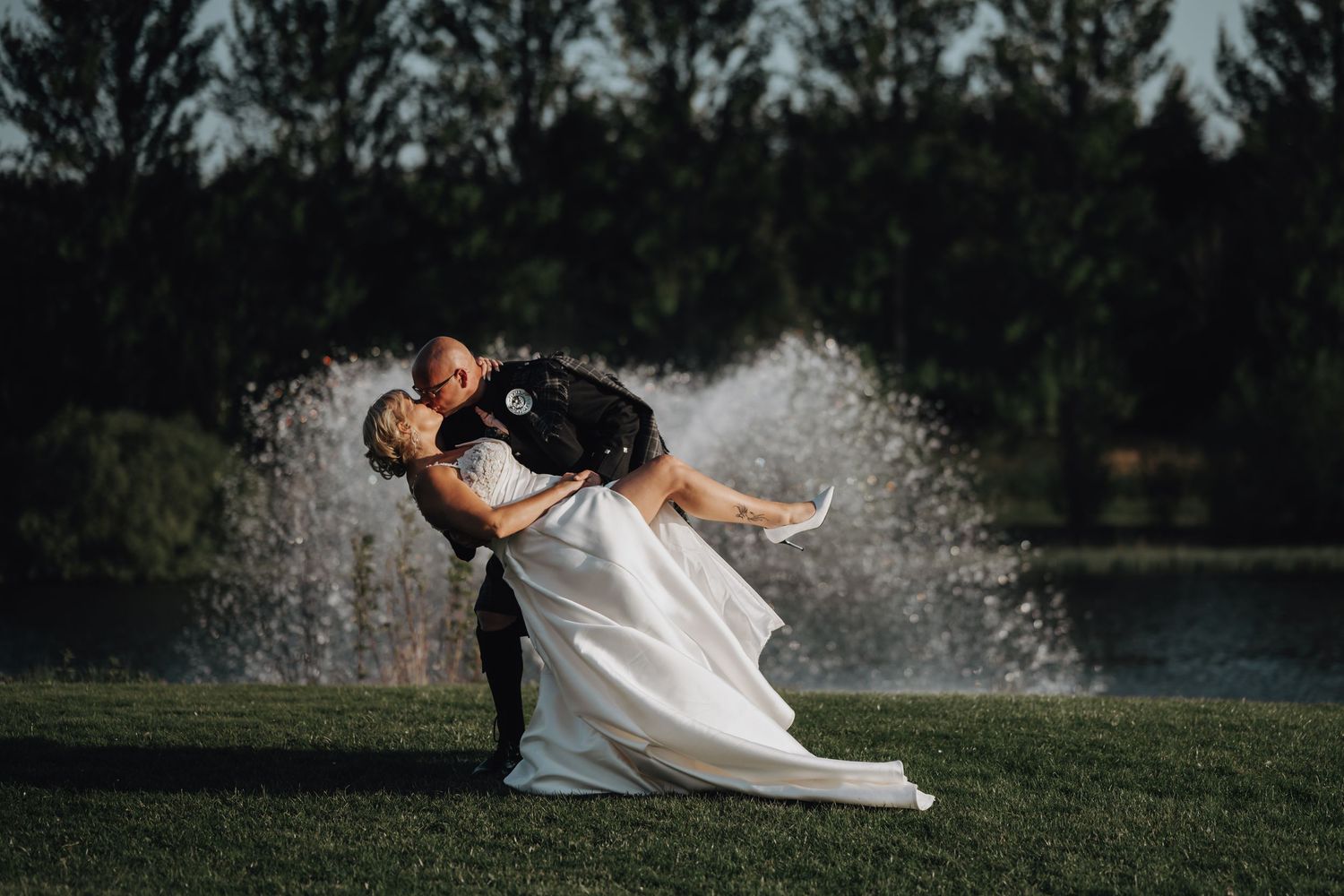 A dramatic dip kiss between newlyweds with water fountain spraying in the background.
