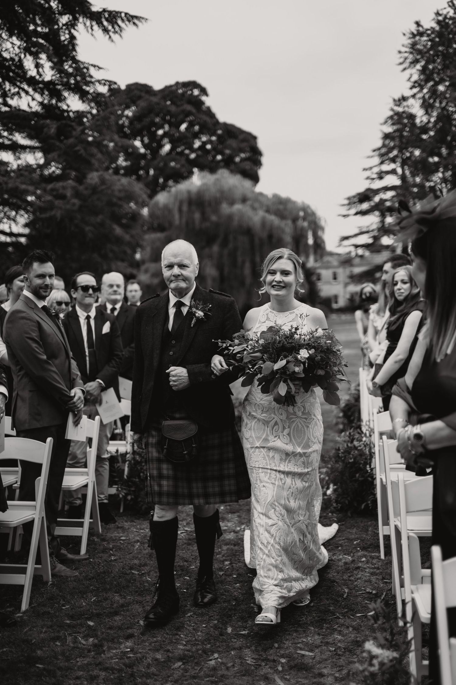 Black and white photo series showing progression of bride walking down outdoor wedding aisle with guests looking on.