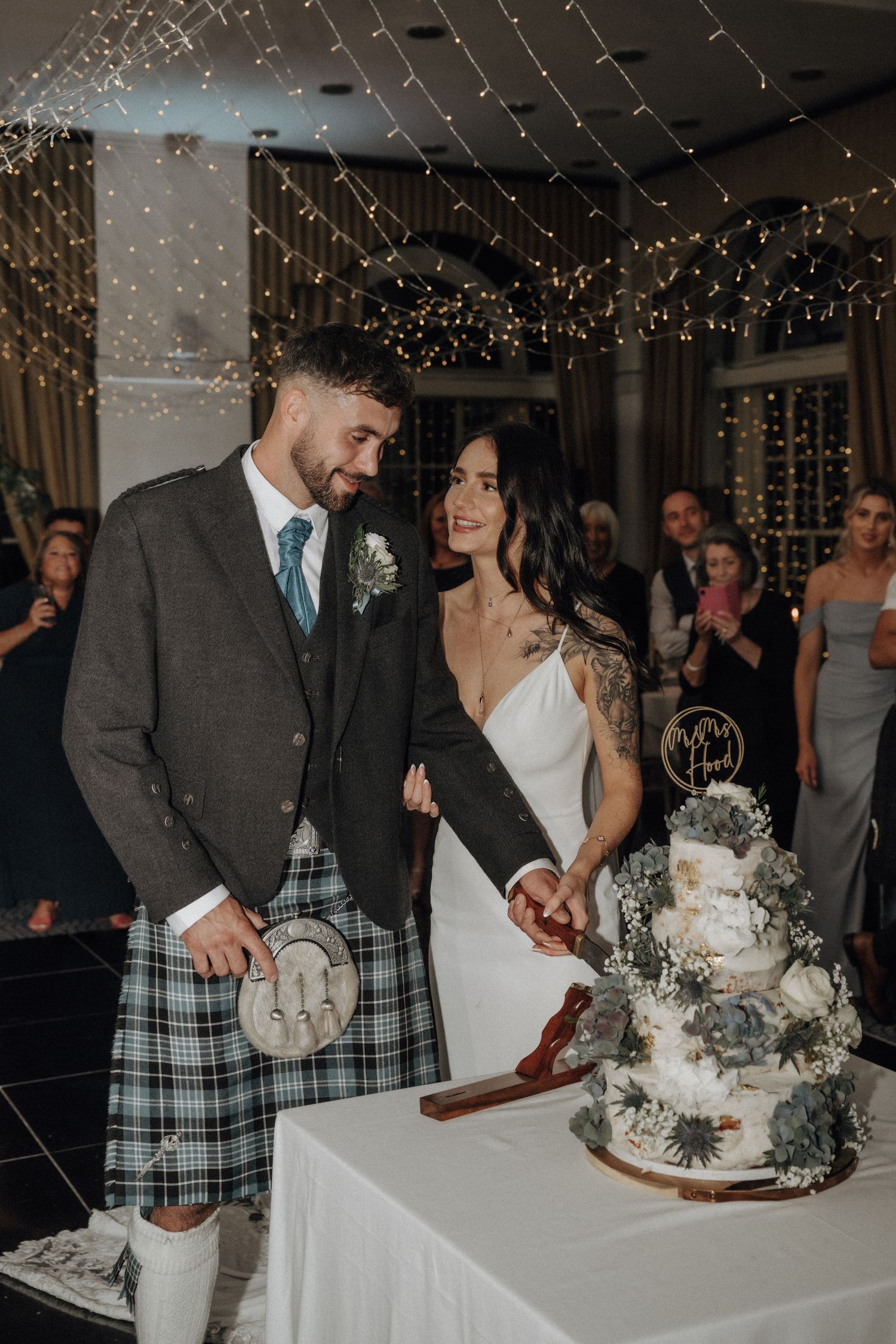 Couple cutting their elegant wedding cake under ceiling fairy lights.