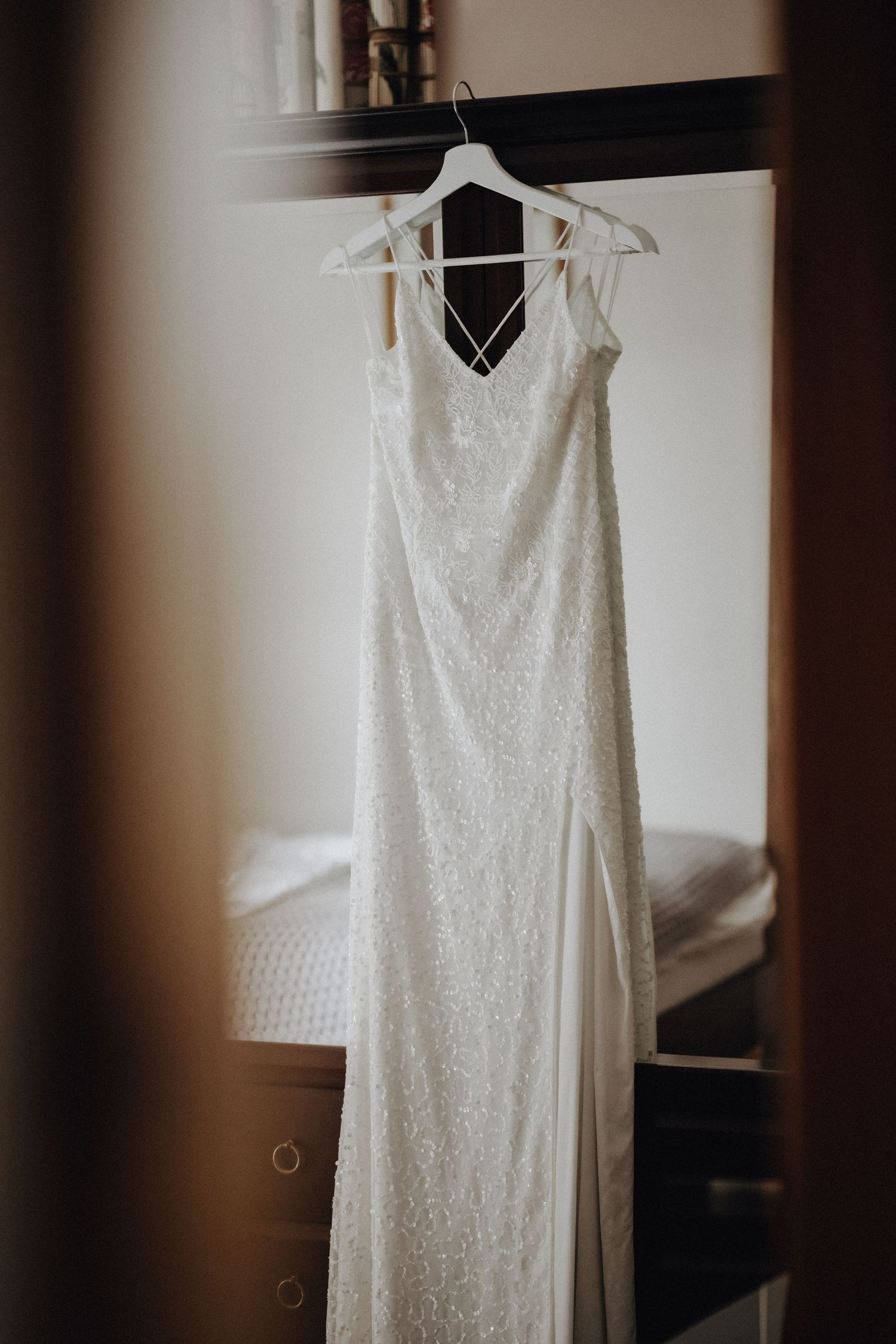 Elegant white lace wedding dress hanging on display against light wall.