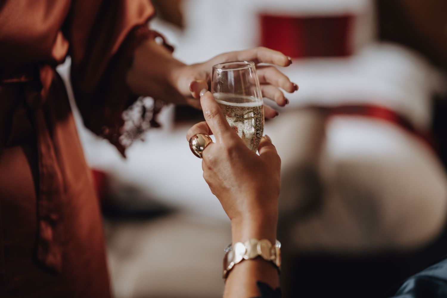 Hand holding champagne glass with elegant bracelet watch during wedding preparations.