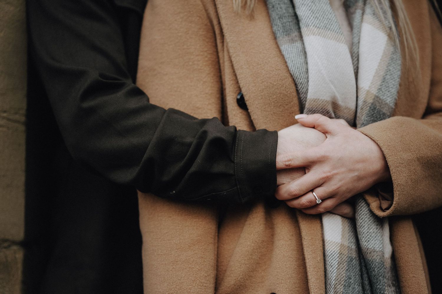 Detail shot of hands embracing through cozy winter coats during romantic moment.