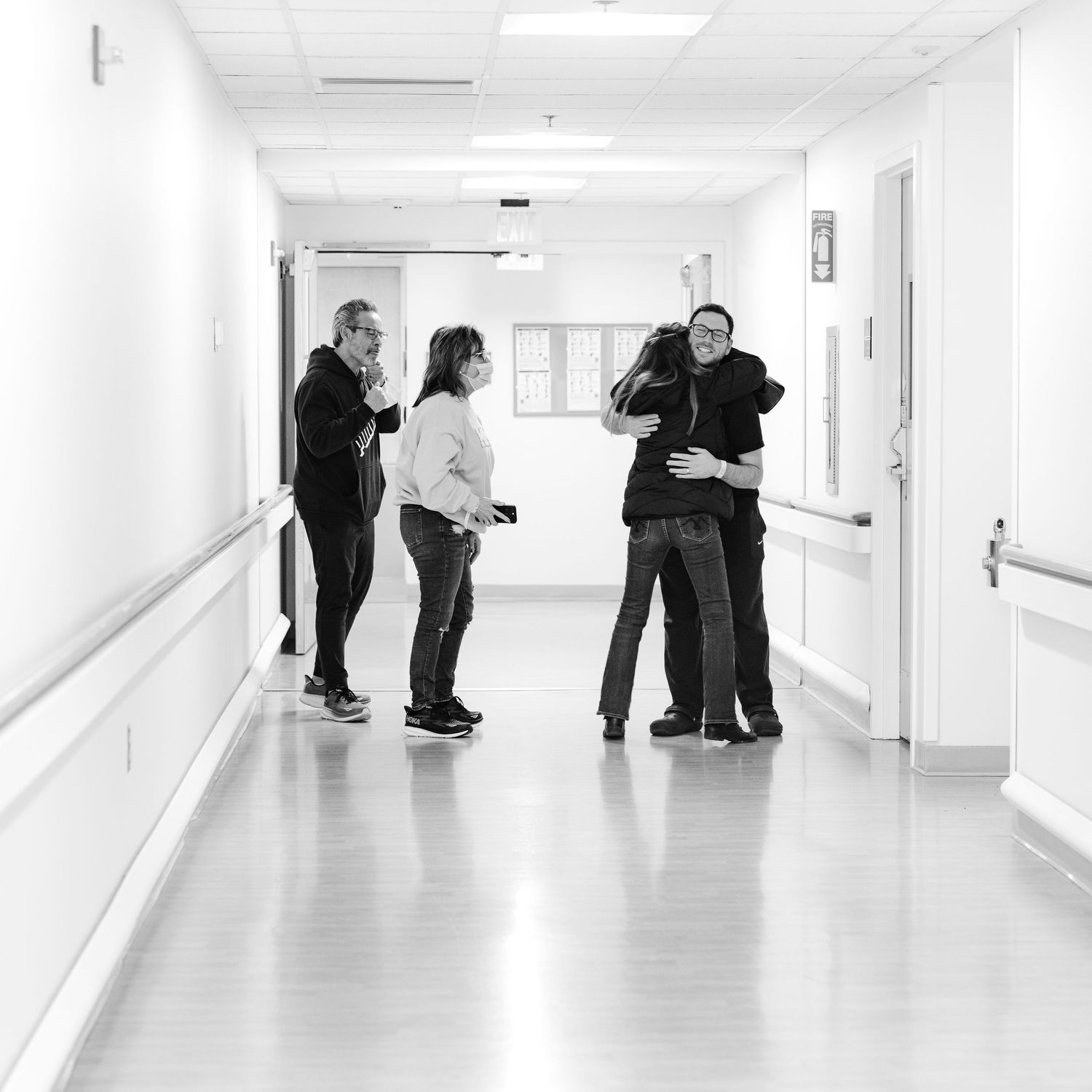 Black and white photo of people hugging and talking in a bright hospital corridor.