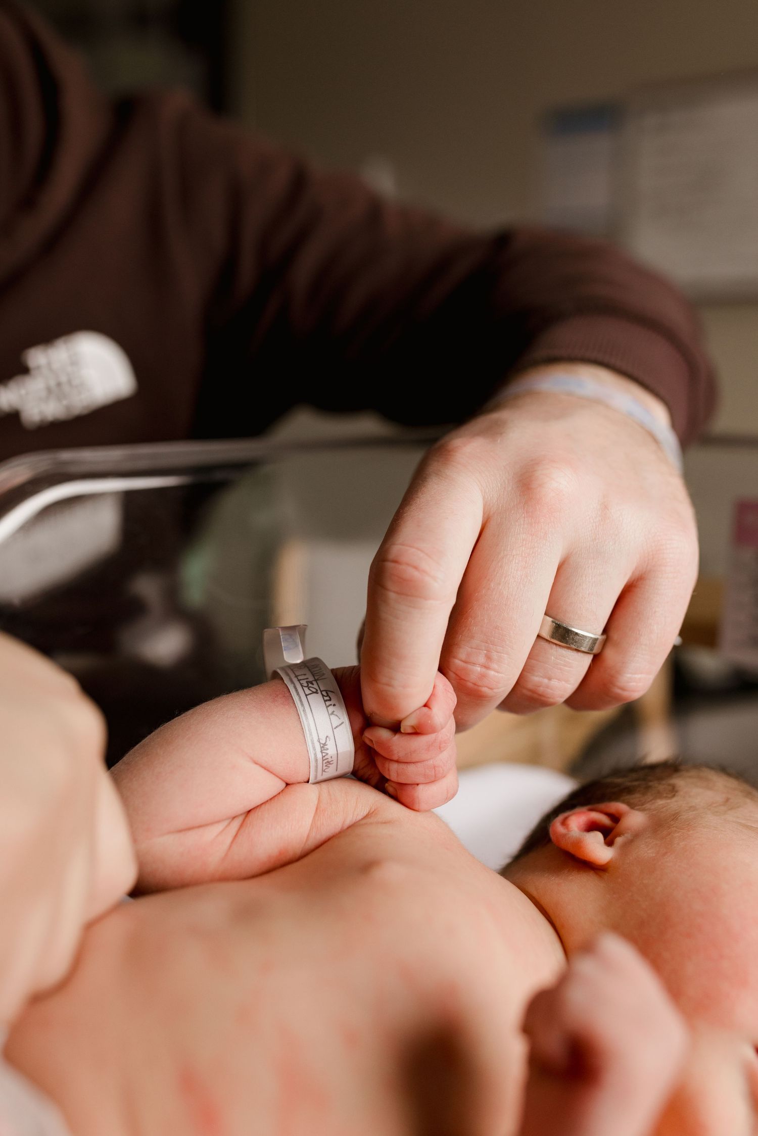 Parent holding newborn baby's tiny hand in hospital, baby wearing ID bracelet, touching family moment.