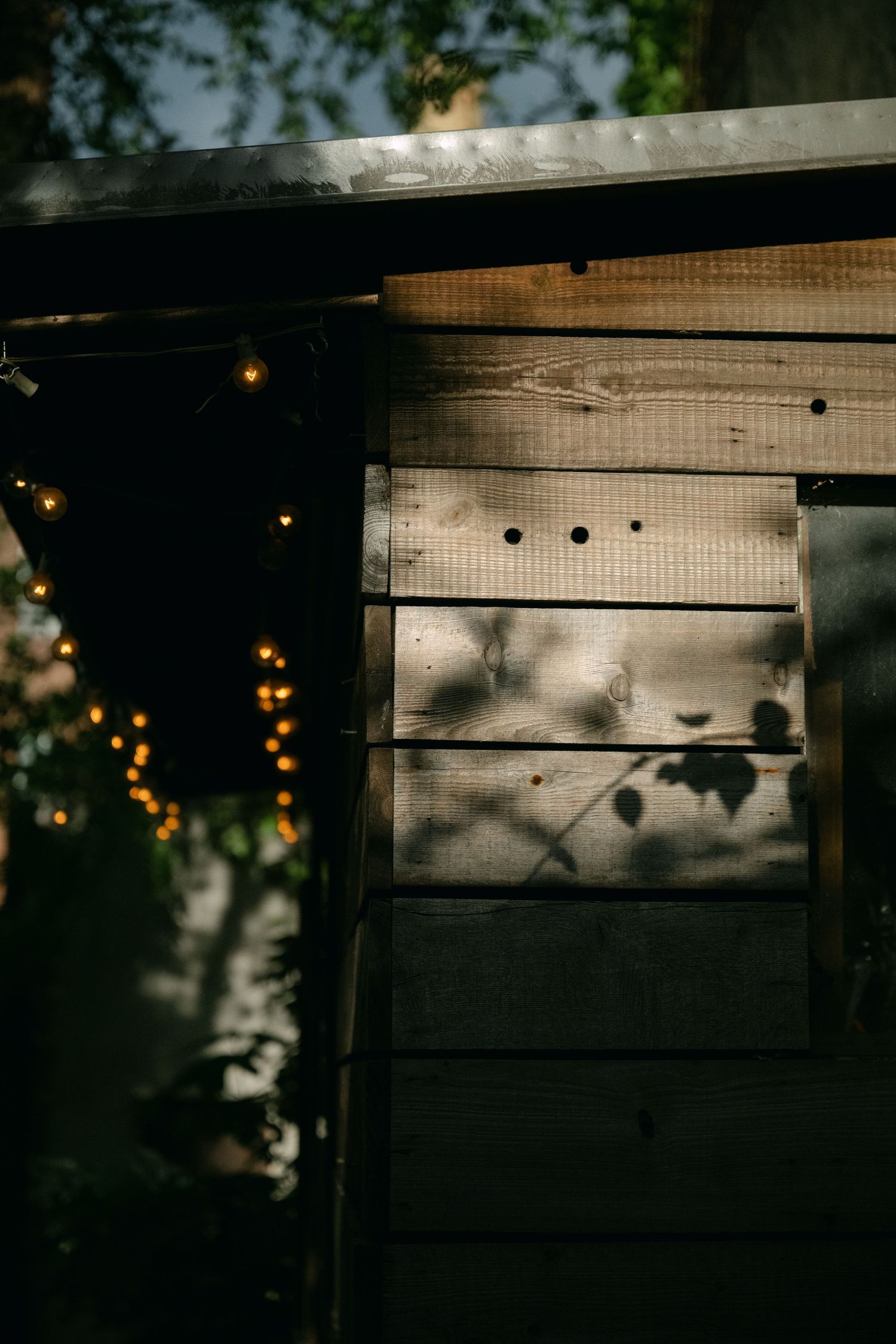 String lights cast a warm glow on rustic wooden wall panels in moody evening shadows.