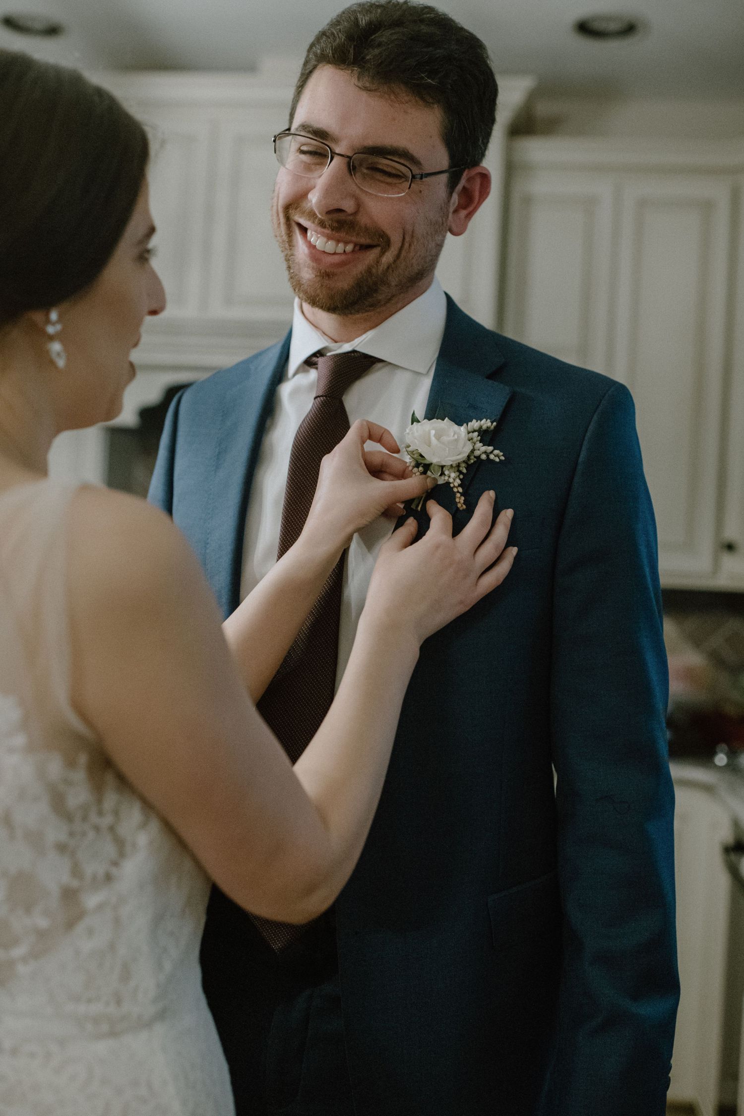An intimate moment as a bride pins a white boutonniere onto her groom's navy suit.