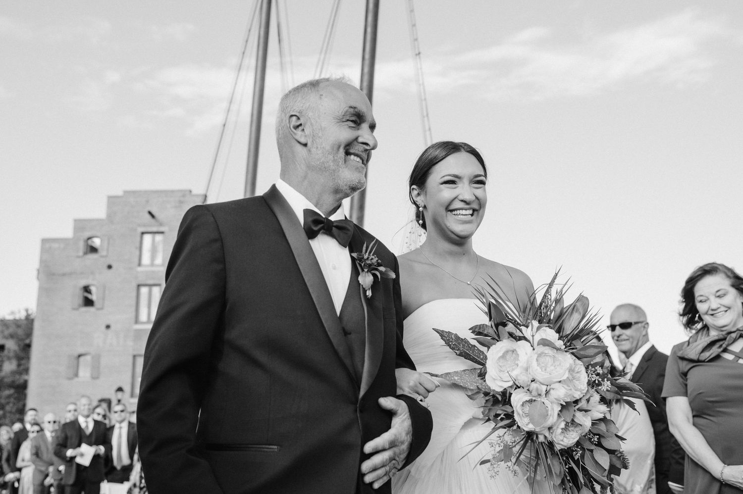 A black and white photo of a joyful moment during an outdoor waterfront wedding ceremony.