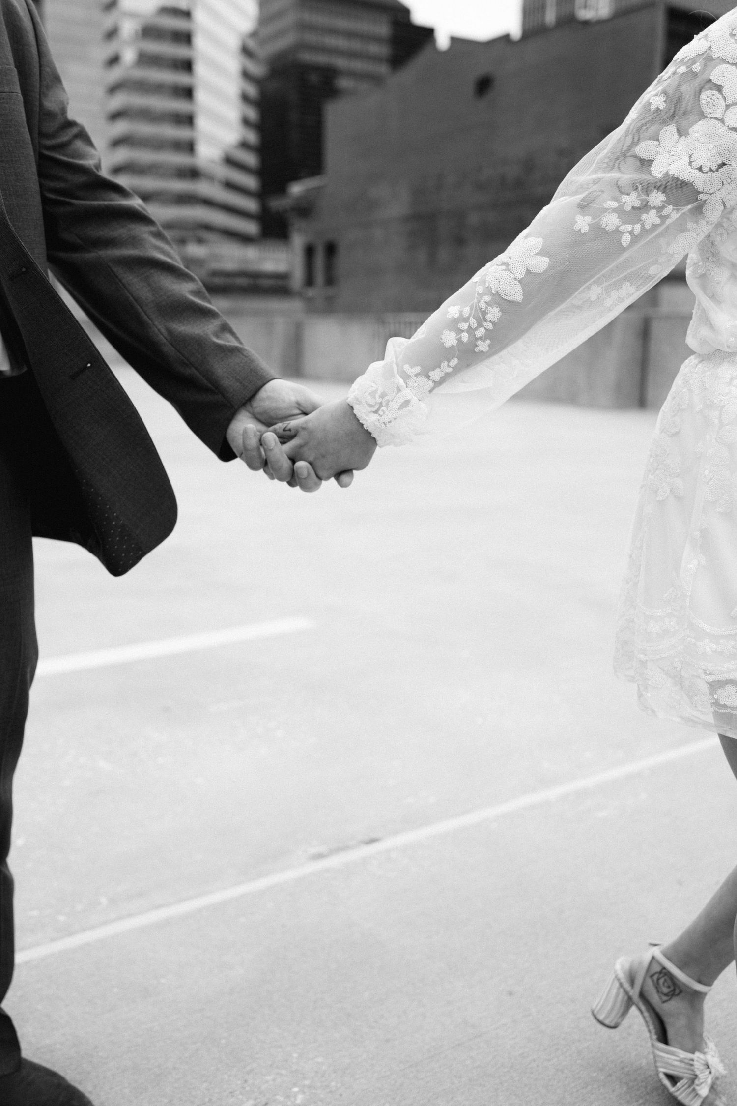 Black and white photo of a couple holding hands, showing lace dress sleeve details and formal attire.