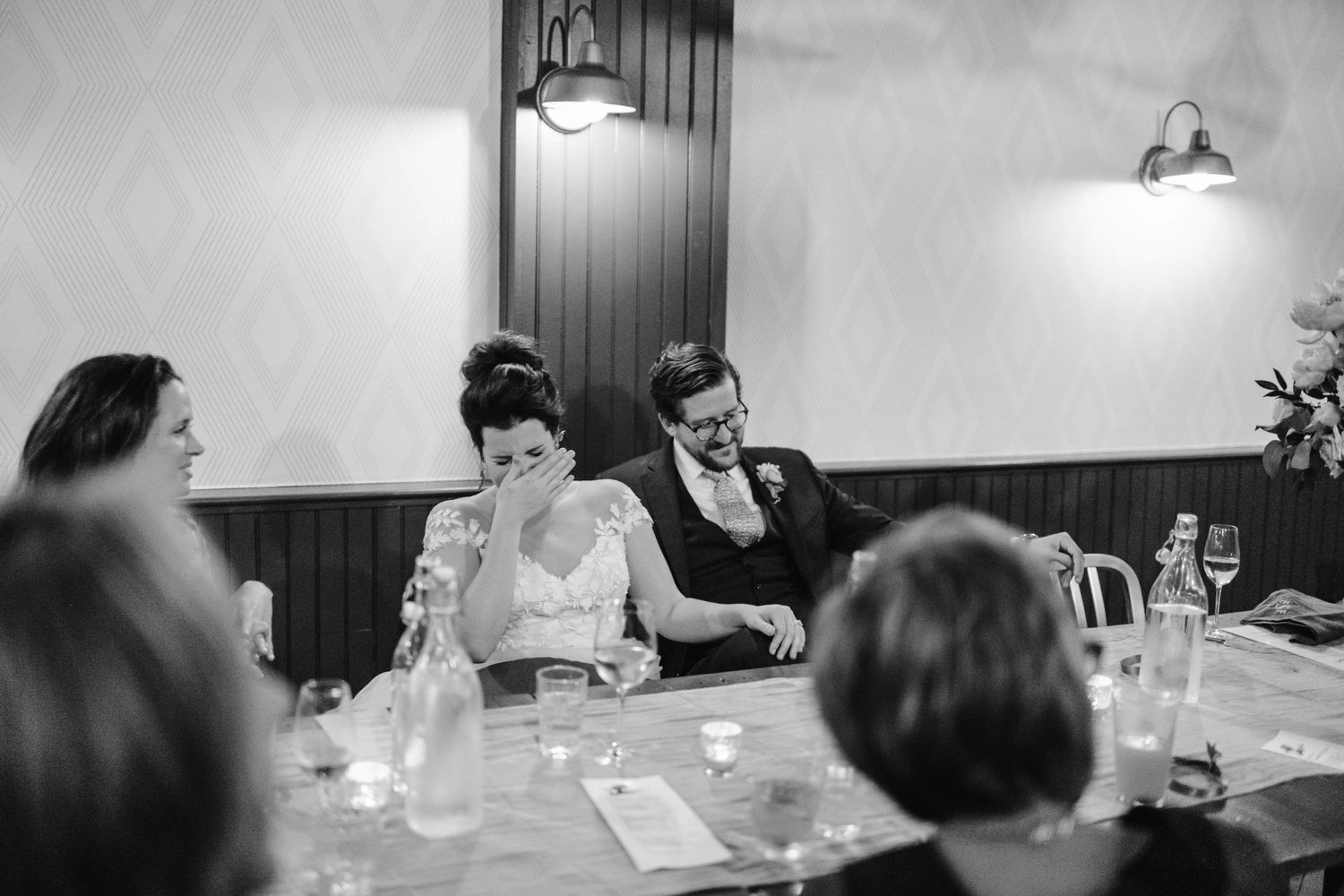 Black and white candid photo of wedding guests enjoying conversation at a reception dinner.