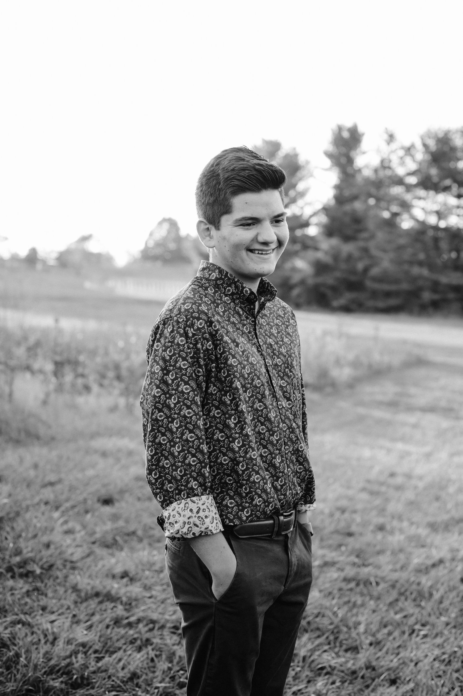 Black and white portrait of a young person smiling outdoors wearing a patterned sweater.