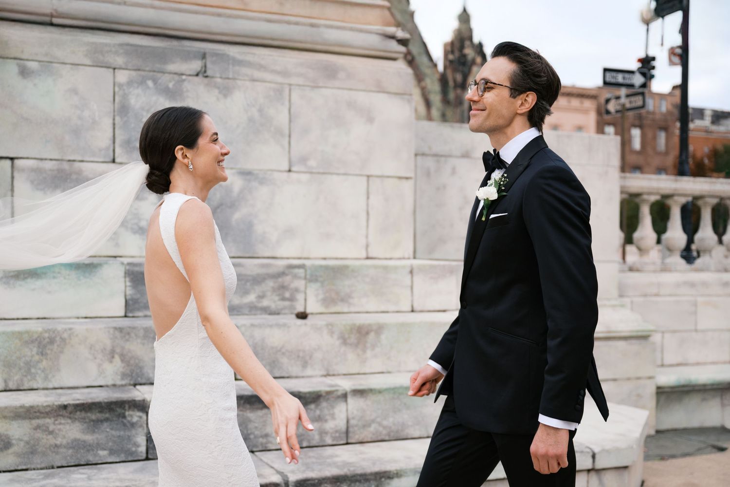 A bride in white and groom in black share a moment on marble steps during their wedding.