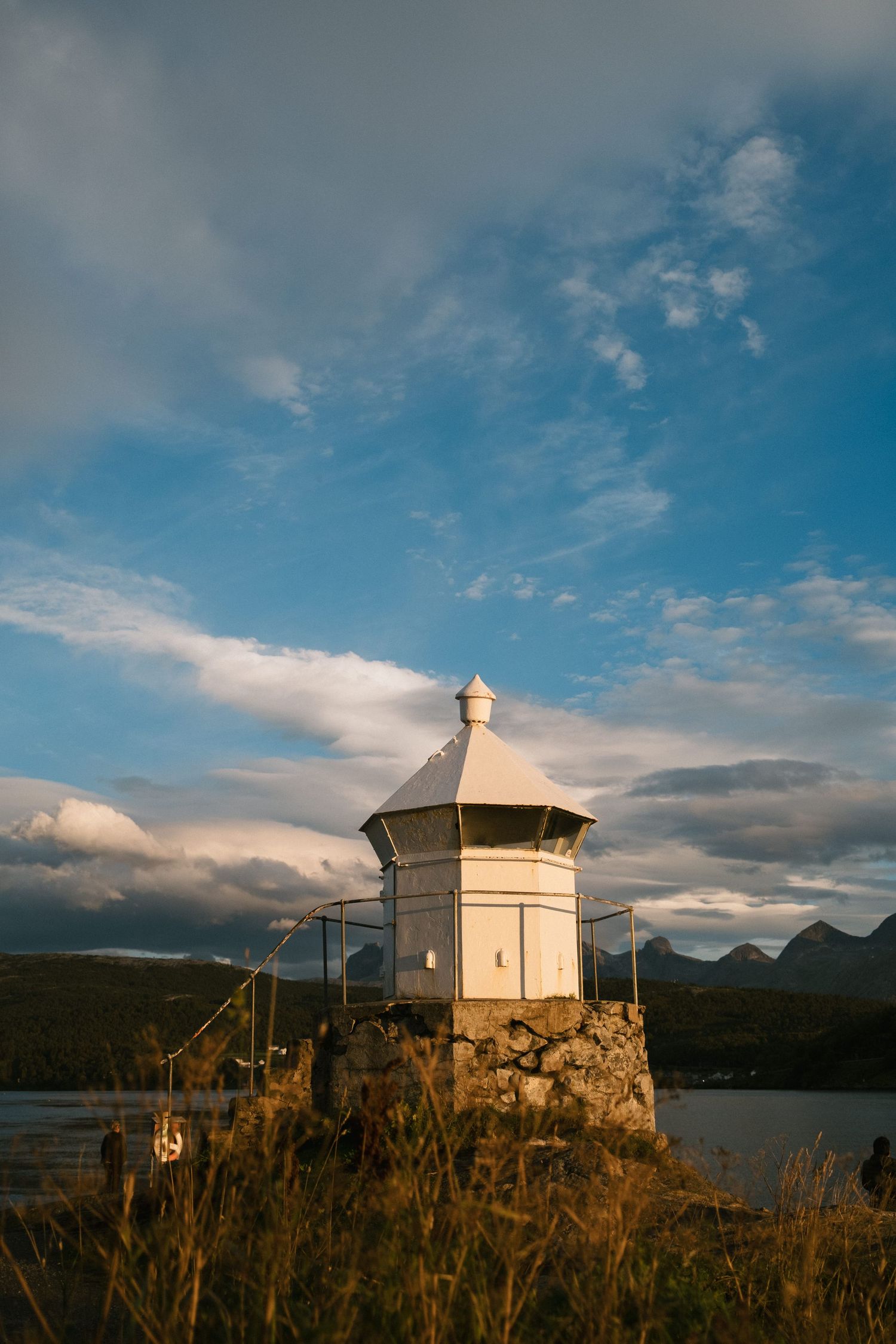 White lighthouse tower perched on rocky outcrop against blue sky with clouds.