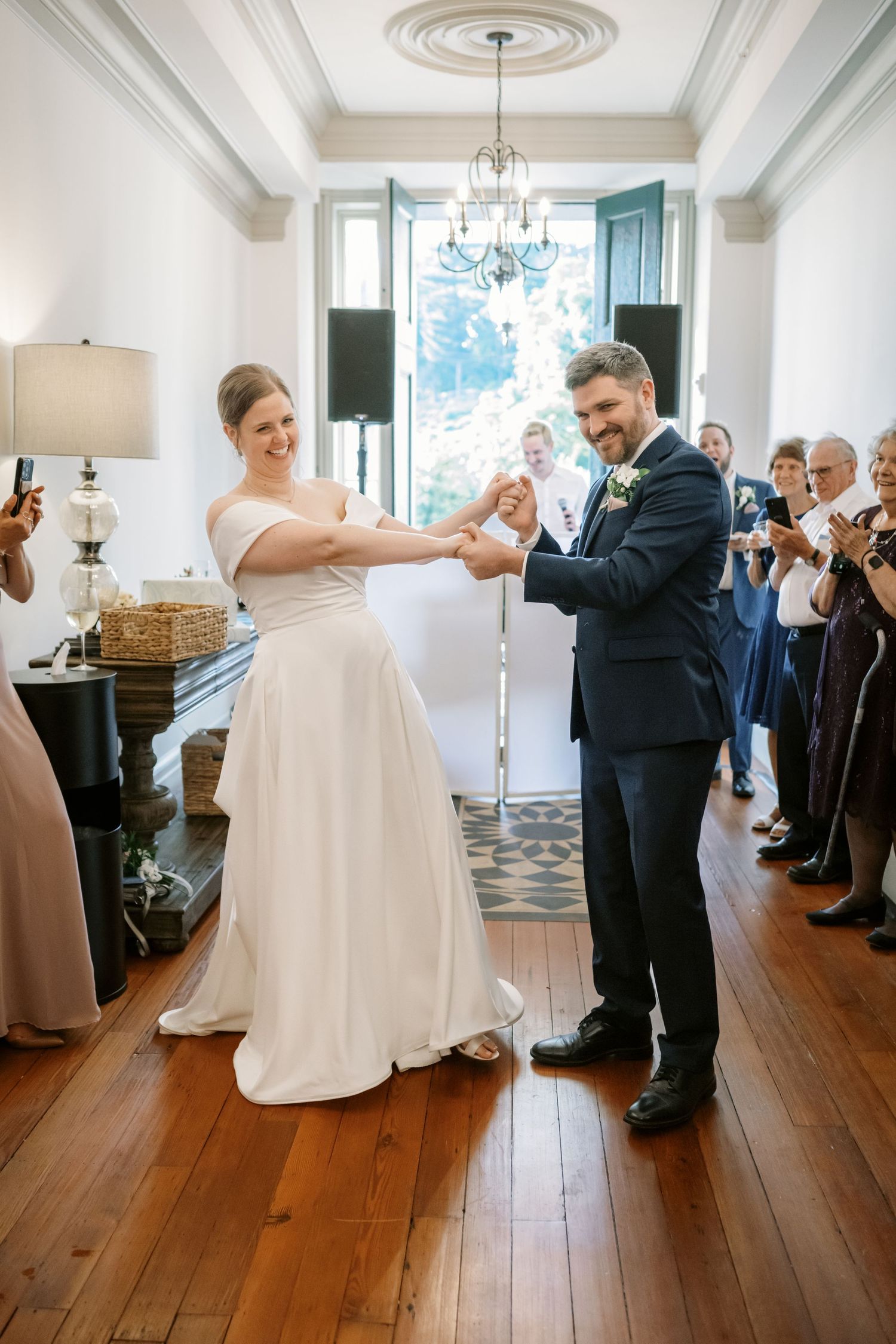 Newlyweds sharing a playful dance moment on hardwood floors while guests applaud.