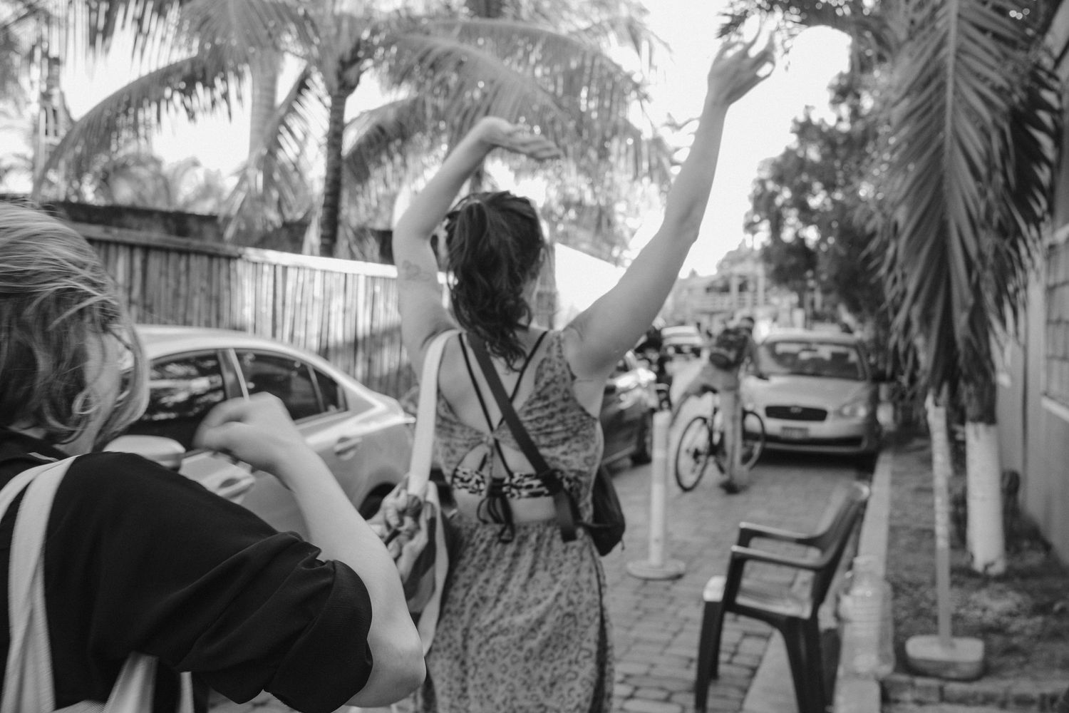 Person raising their hand while taking photos on a palm-tree lined street.