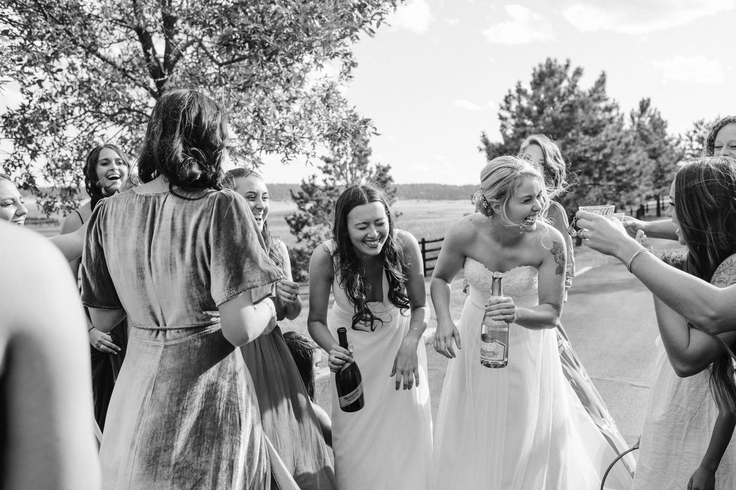 Wedding party laughing and celebrating outdoors on a sunny day.