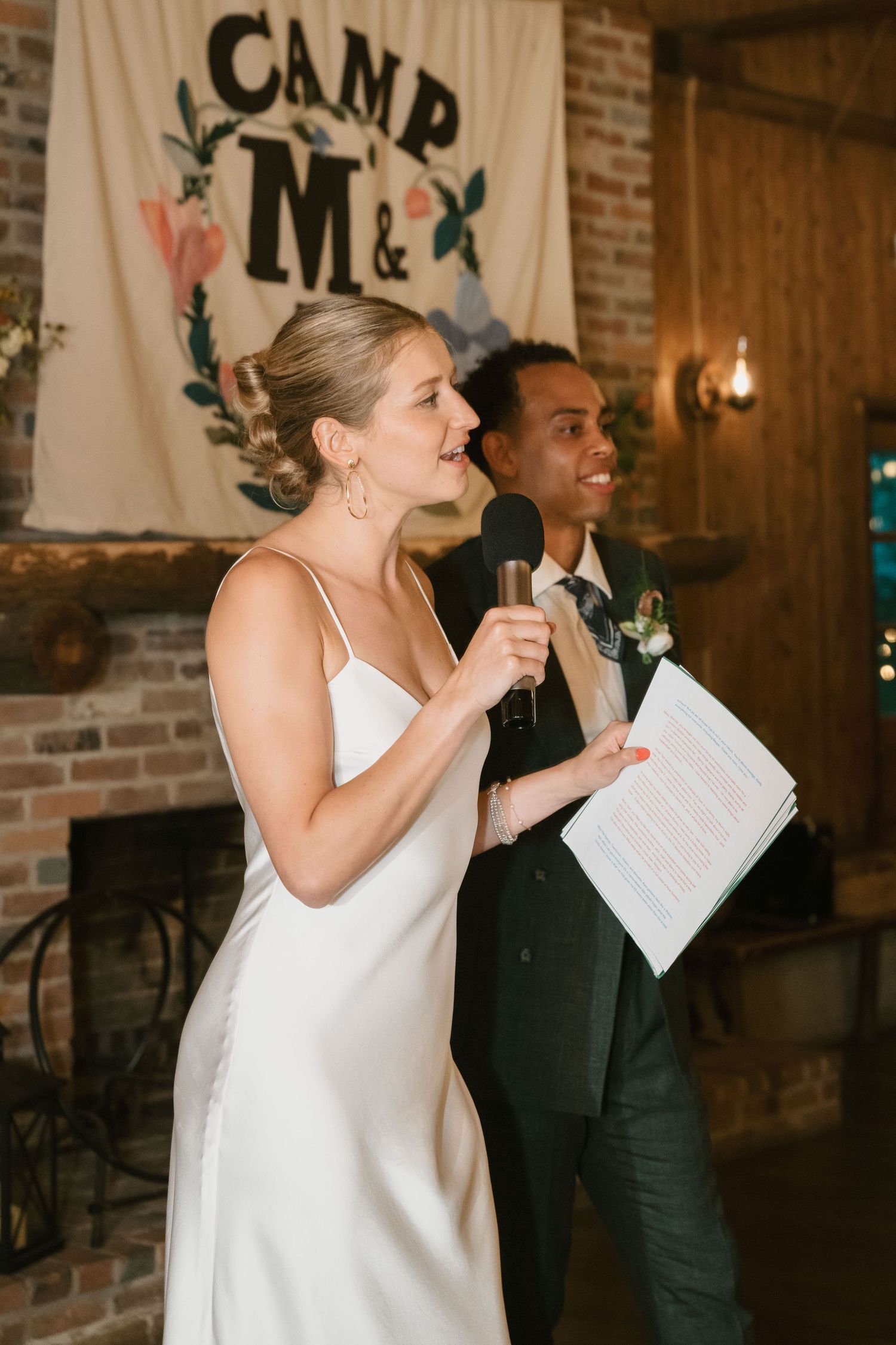Wedding celebration speeches in front of rustic brick fireplace with decorative banner.