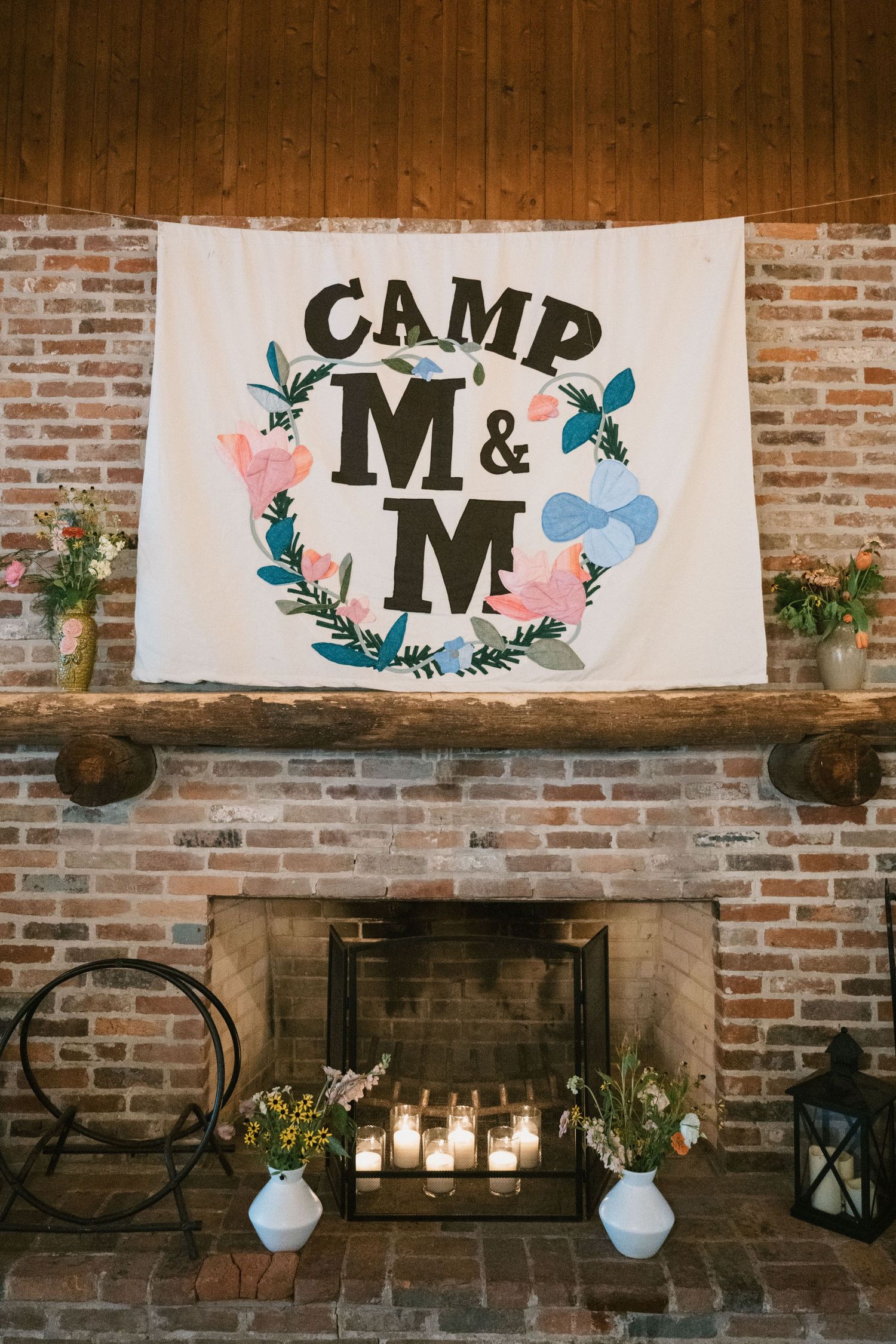 Camp M&M banner with floral design hanging above a brick fireplace with candle decorations.