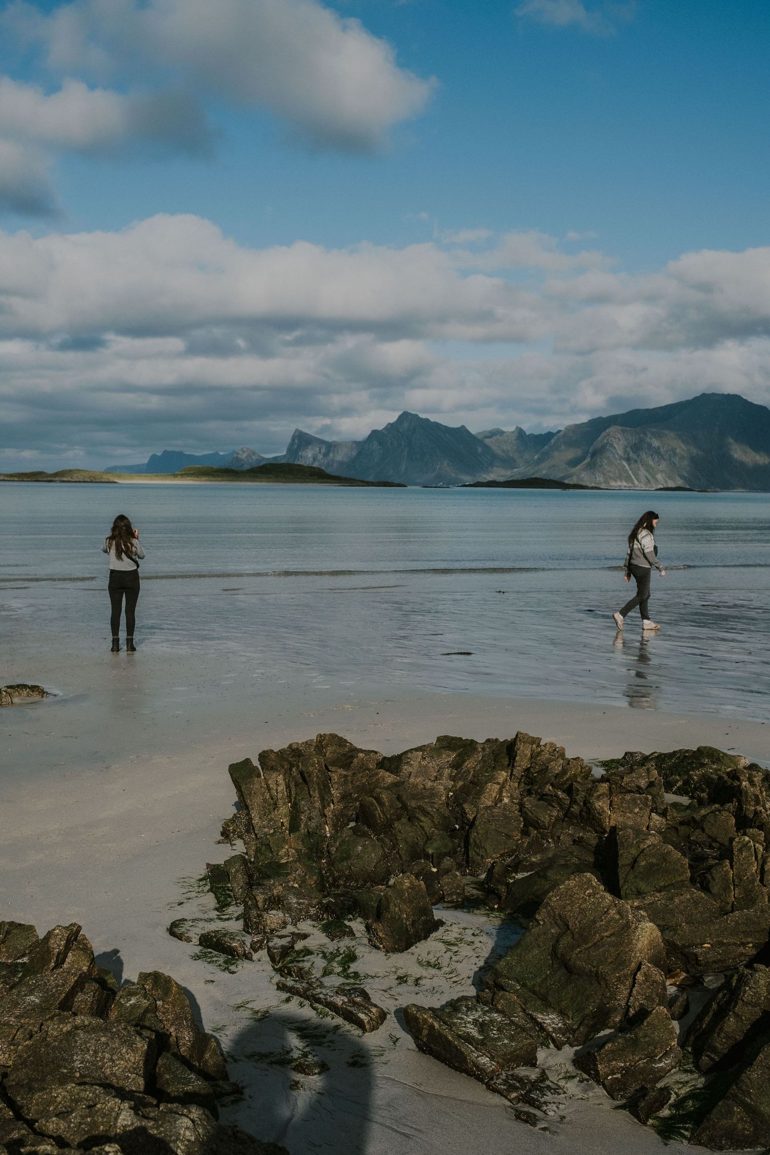 Rocky beach with dramatic mountain backdrop and two figures exploring the shoreline.