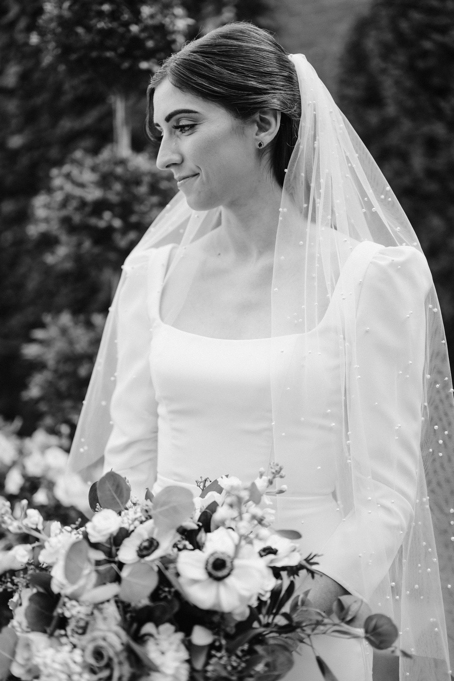 A side profile view of a bride in a classic white dress and veil holding a floral bouquet.