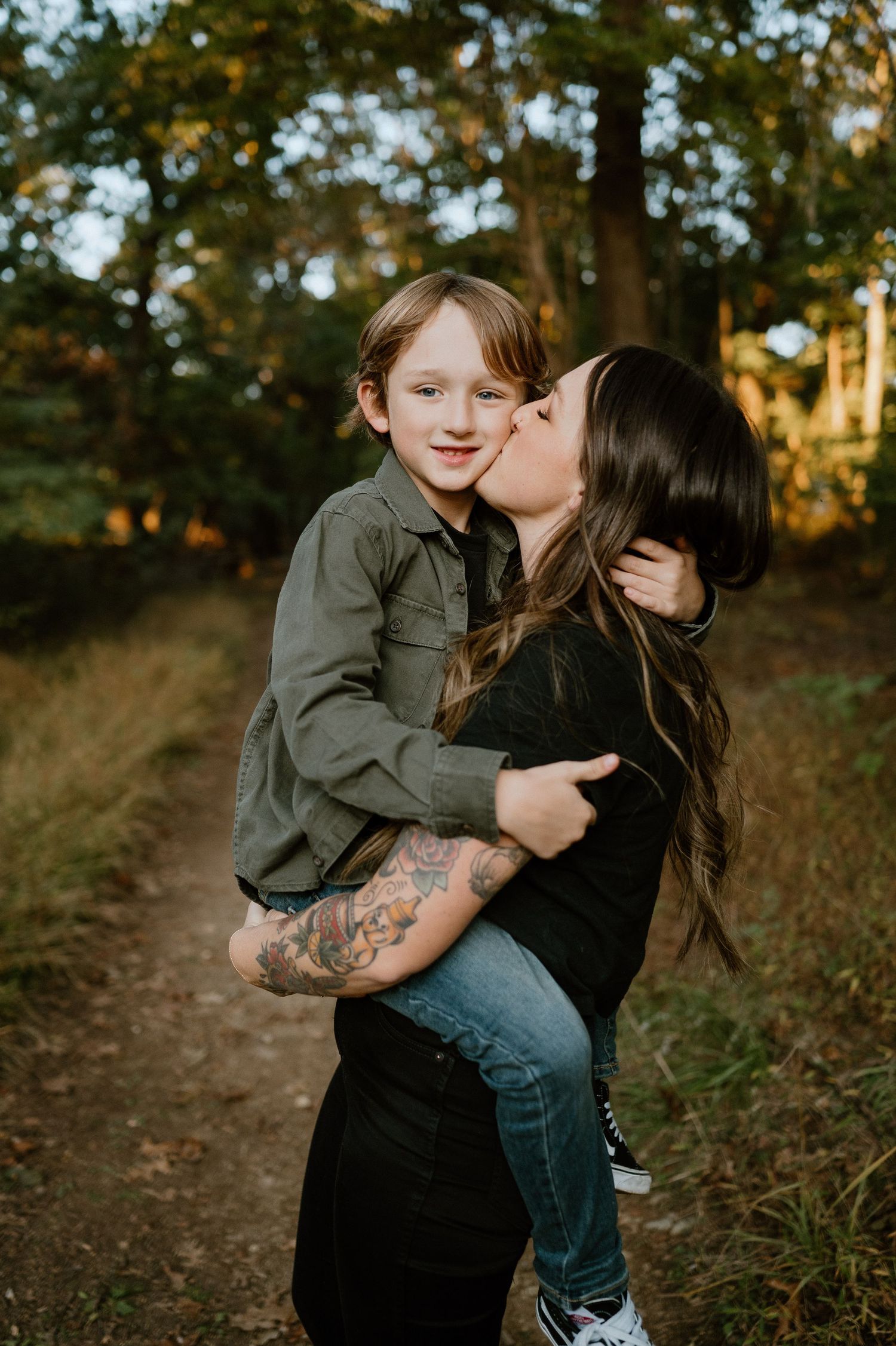 An affectionate embrace between two people captured in golden hour lighting on a wooded path.