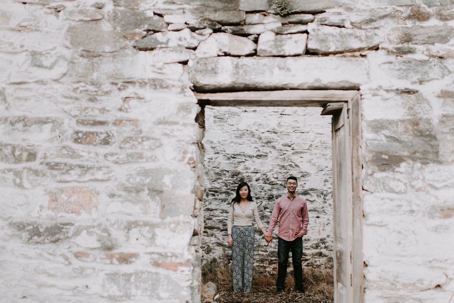 Two people stand framed within a stone doorway of an old rustic building.