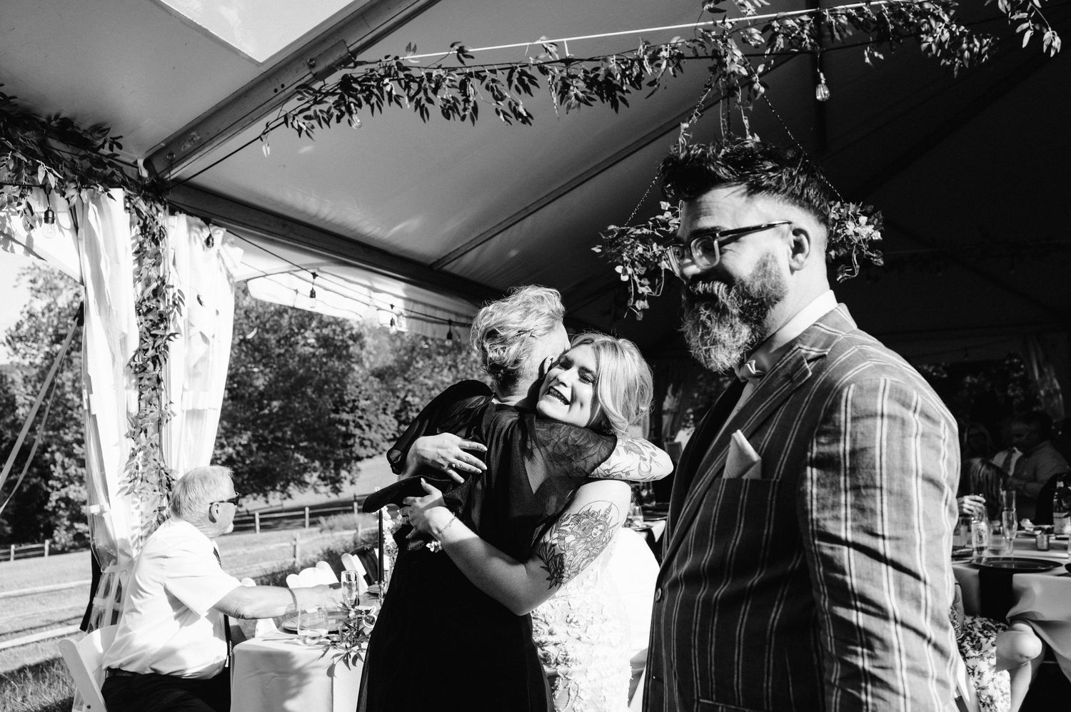Wedding guests gather for group photo under decorated tent during outdoor celebration.