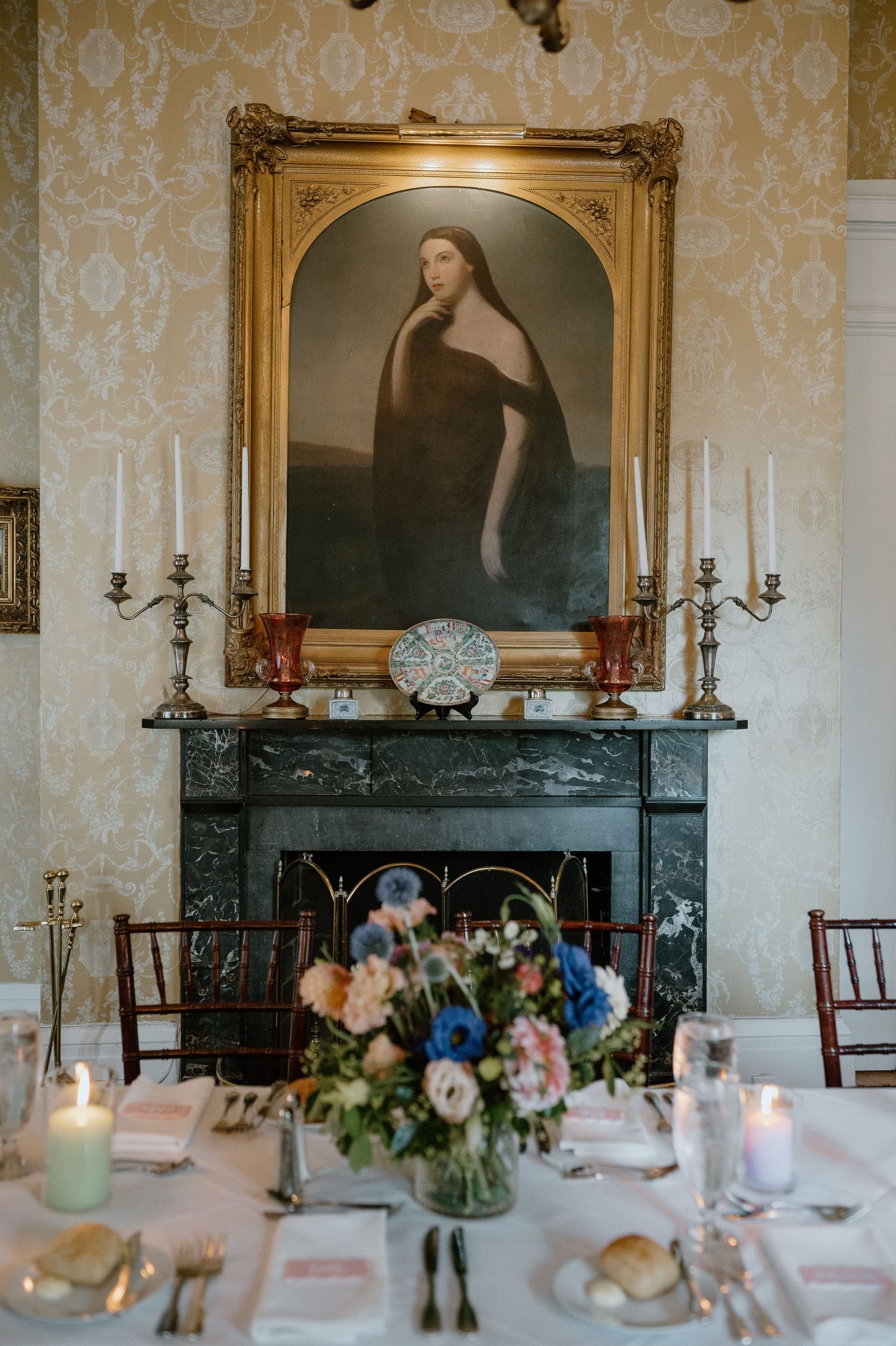 Ornate fireplace with portrait painting and floral centerpiece in an elegant dining room.