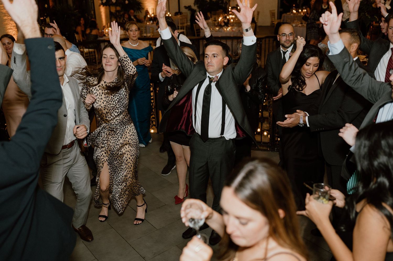 Wedding guests dance enthusiastically on a dark dance floor during an evening reception celebration.