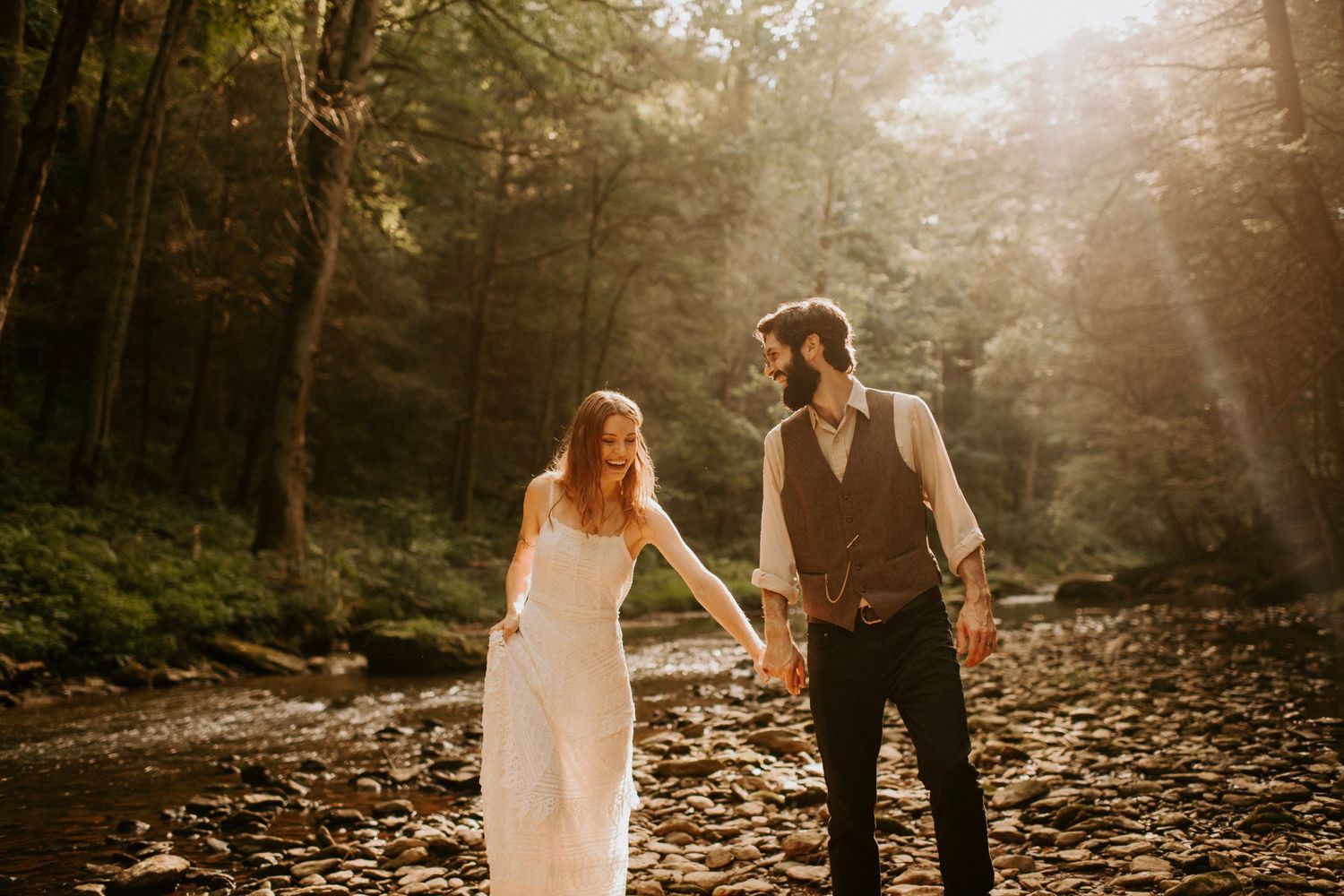 Couple shares intimate moment in sun-dappled forest clearing by stream.