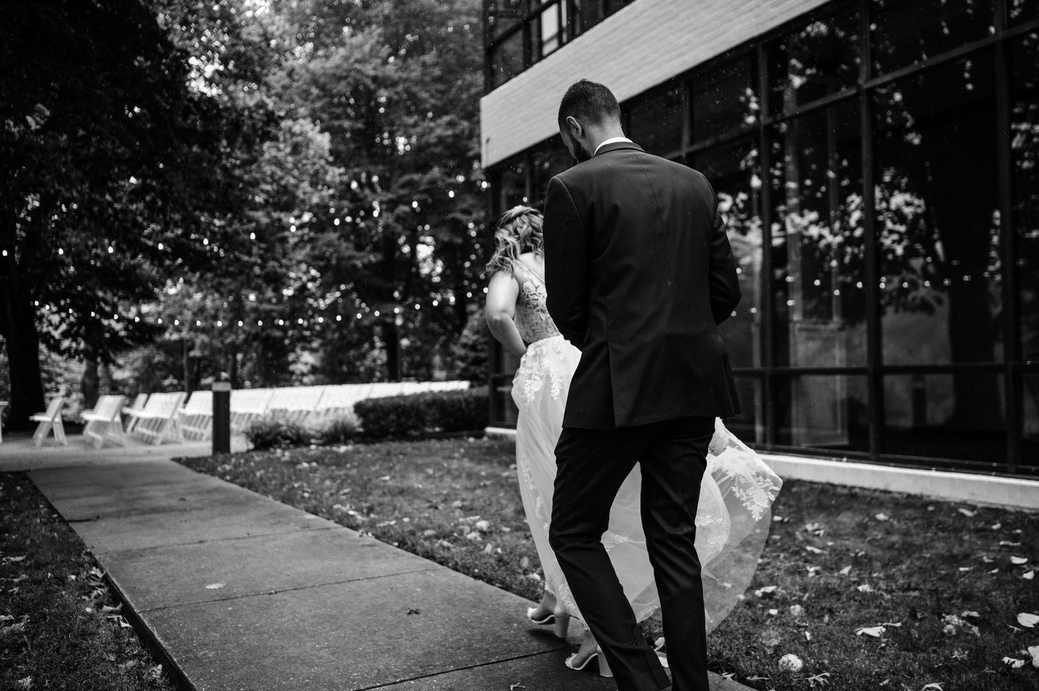 Black and white photo of couple walking together on outdoor pathway after wedding ceremony.