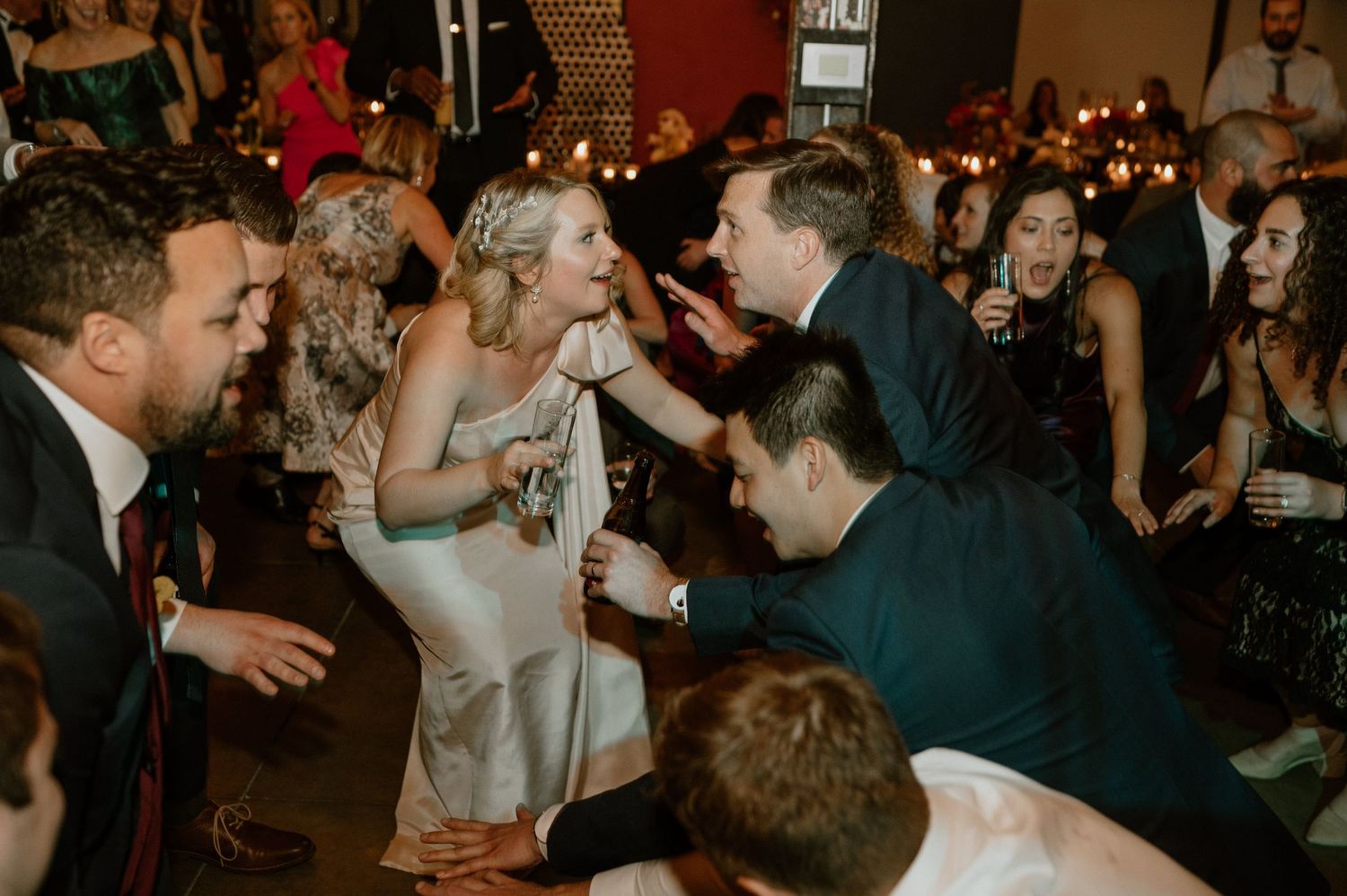 Celebration scene with formal-dressed guests dancing and mingling in a warm-lit venue.