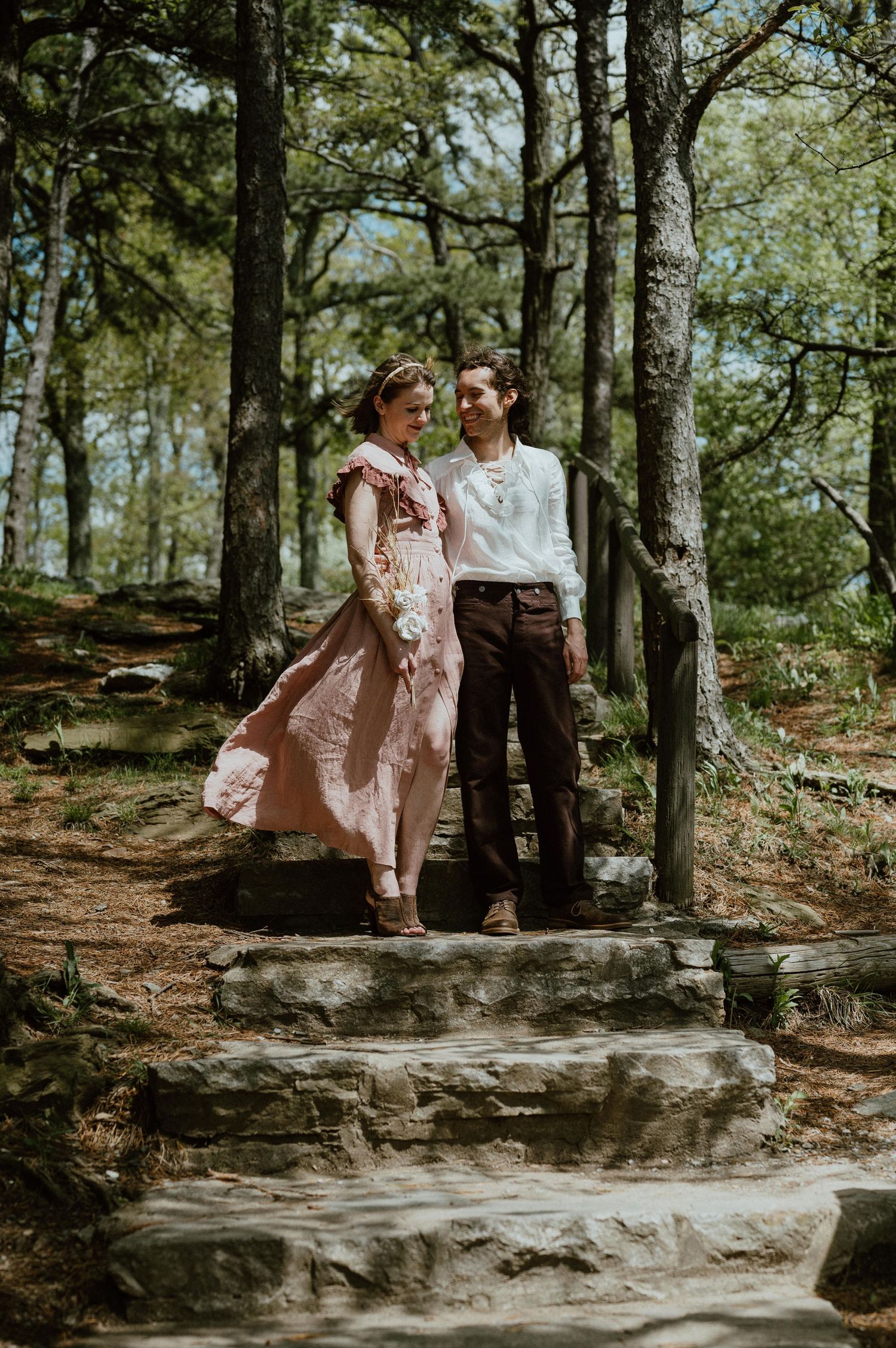Couple posed on stone steps in a forest setting with natural lighting.