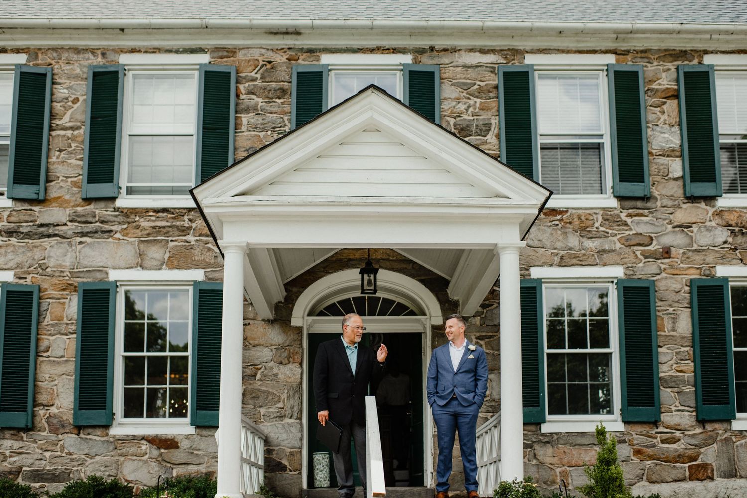Classic stone colonial house facade with white columns and green shutters.