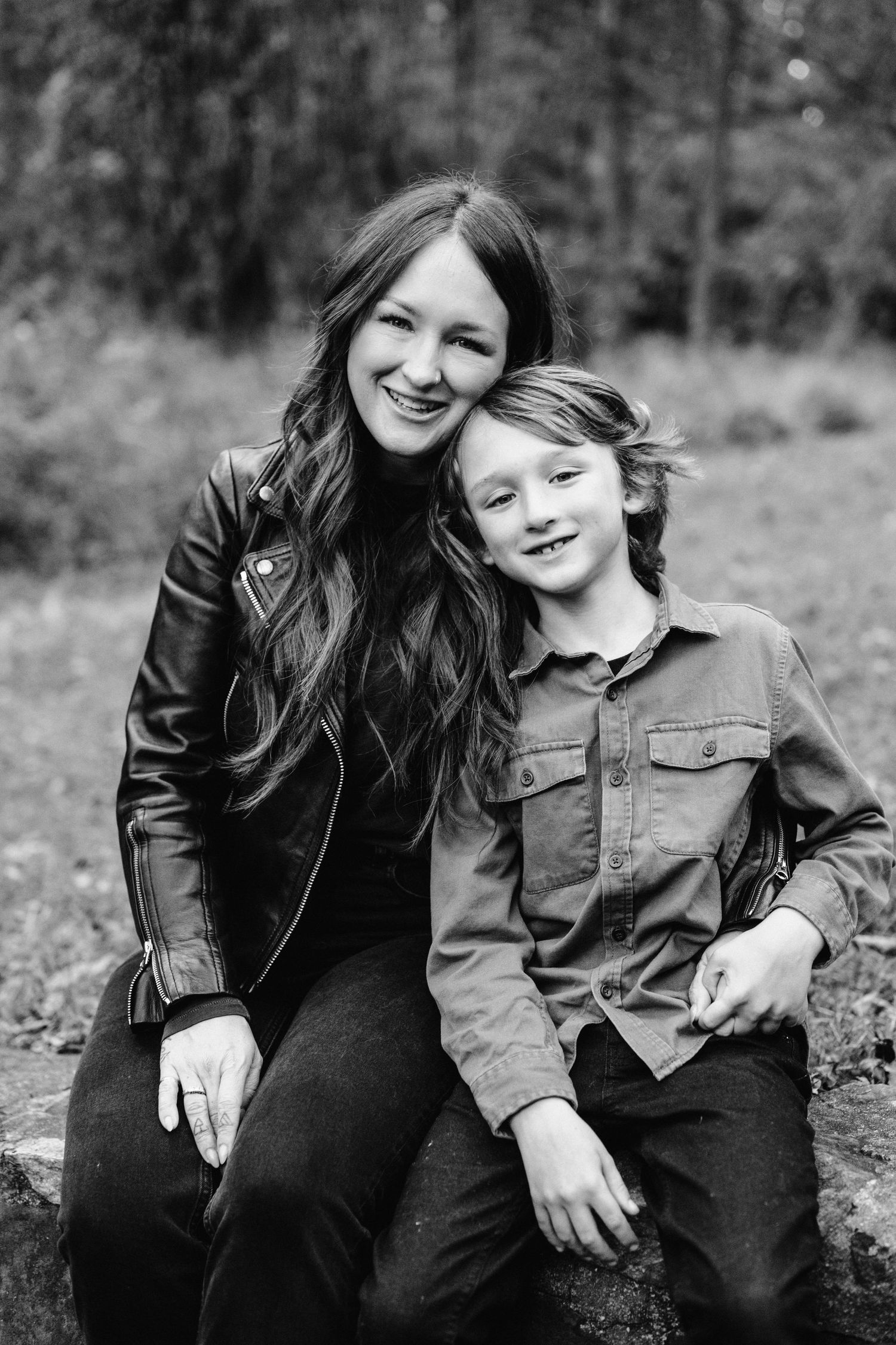 A heartwarming black and white portrait of parent and child sitting together in a casual outdoor setting.