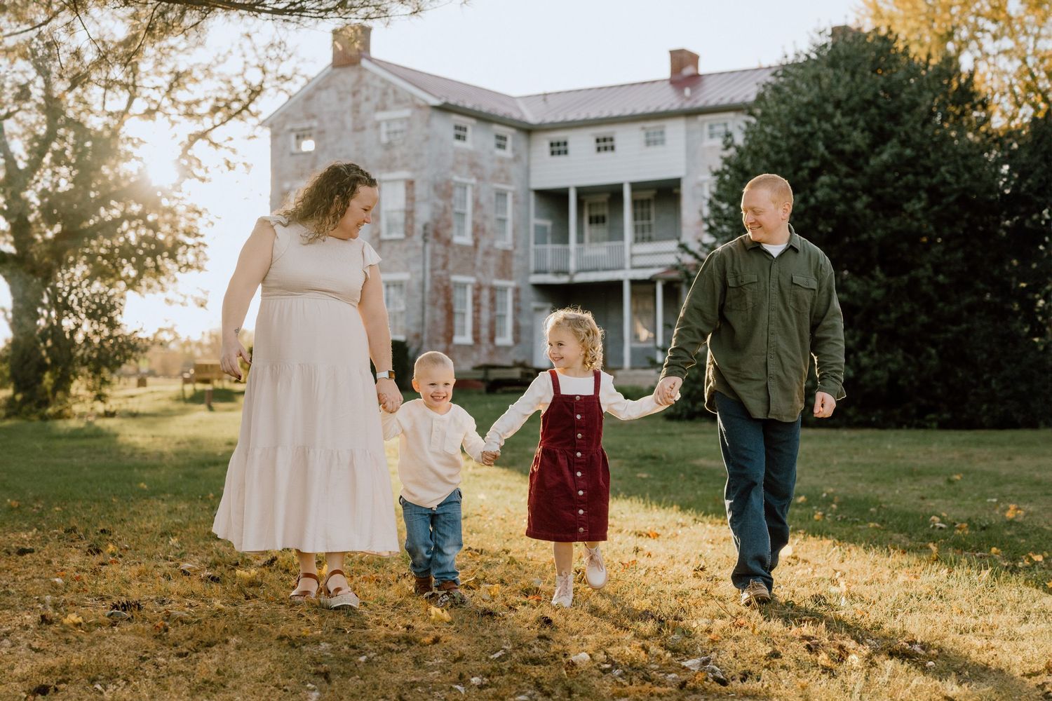 Family holding hands while walking through autumn yard near historic building.