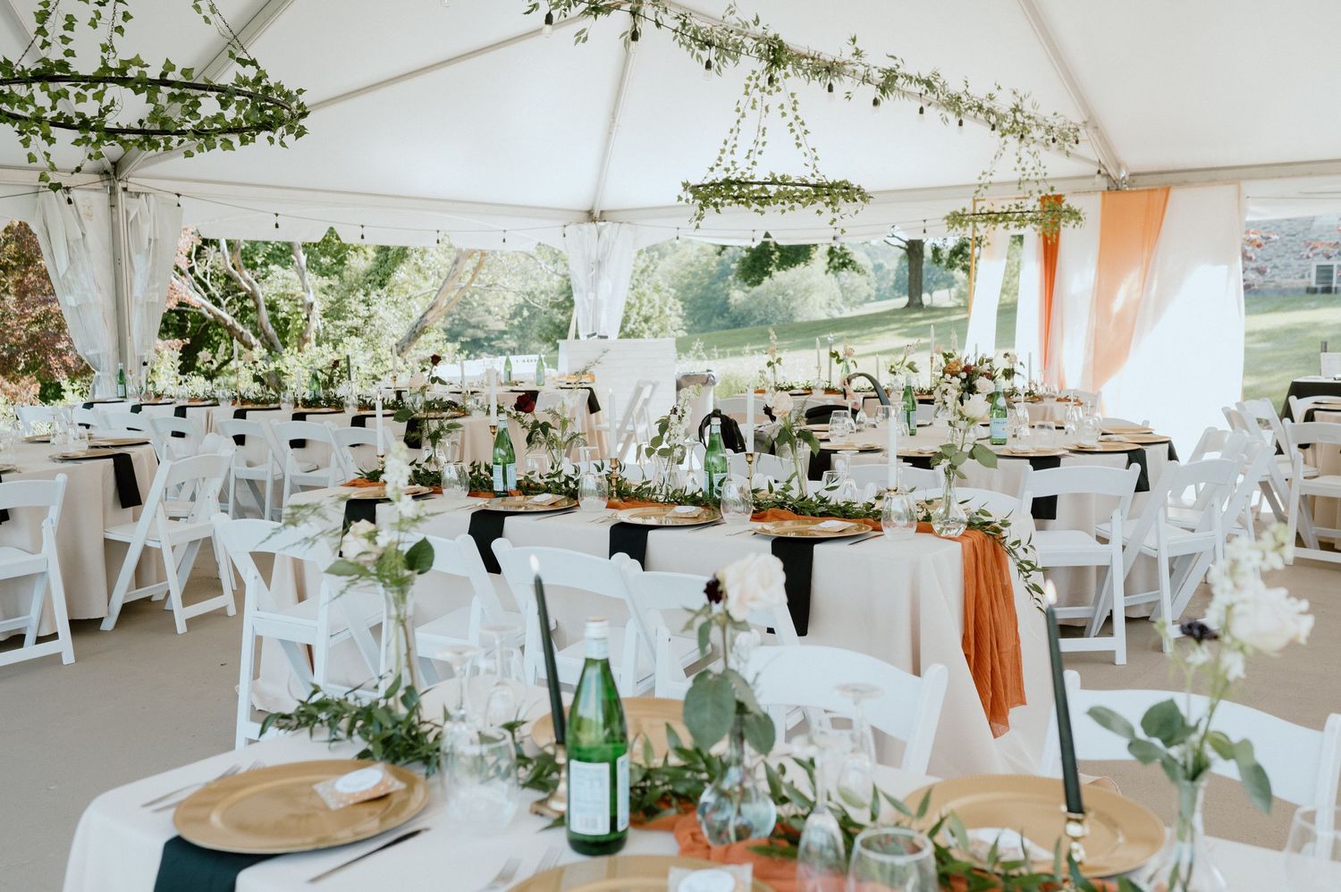 White tent wedding reception with rustic table settings and natural greenery decorations.