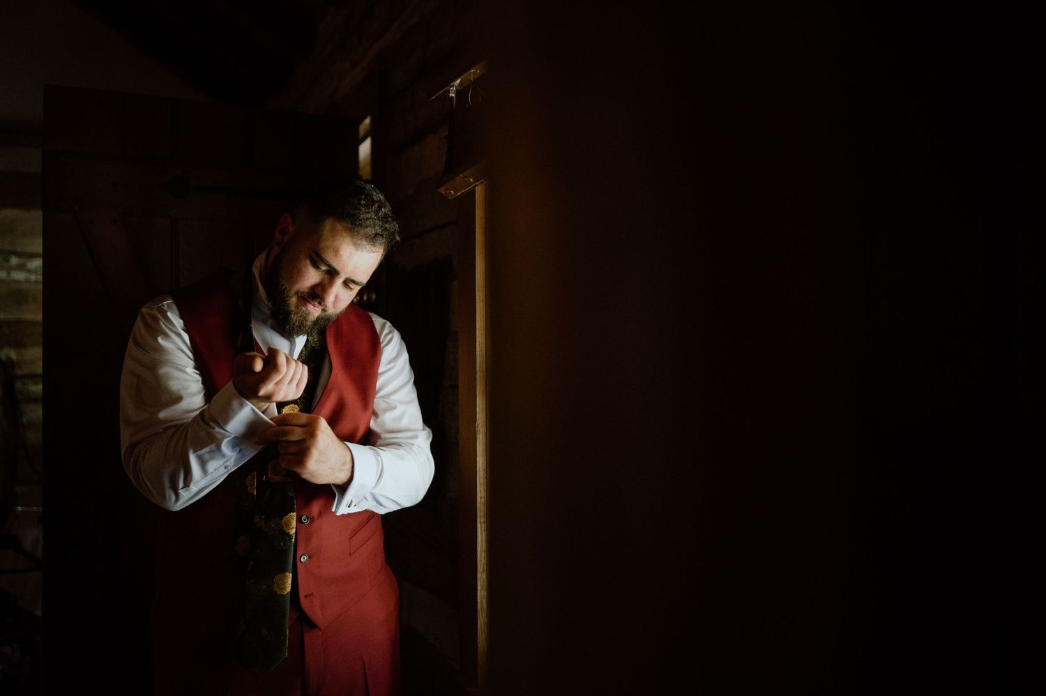 A figure in a red vest adjusts clothing while standing in dramatic shadows.