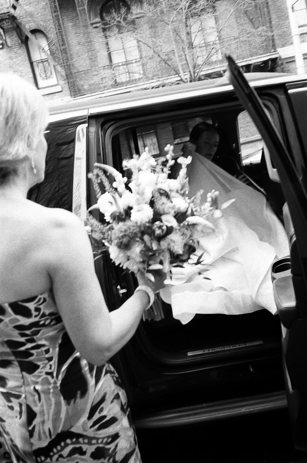 Black and white image of a bridal bouquet with white flowers in a car.