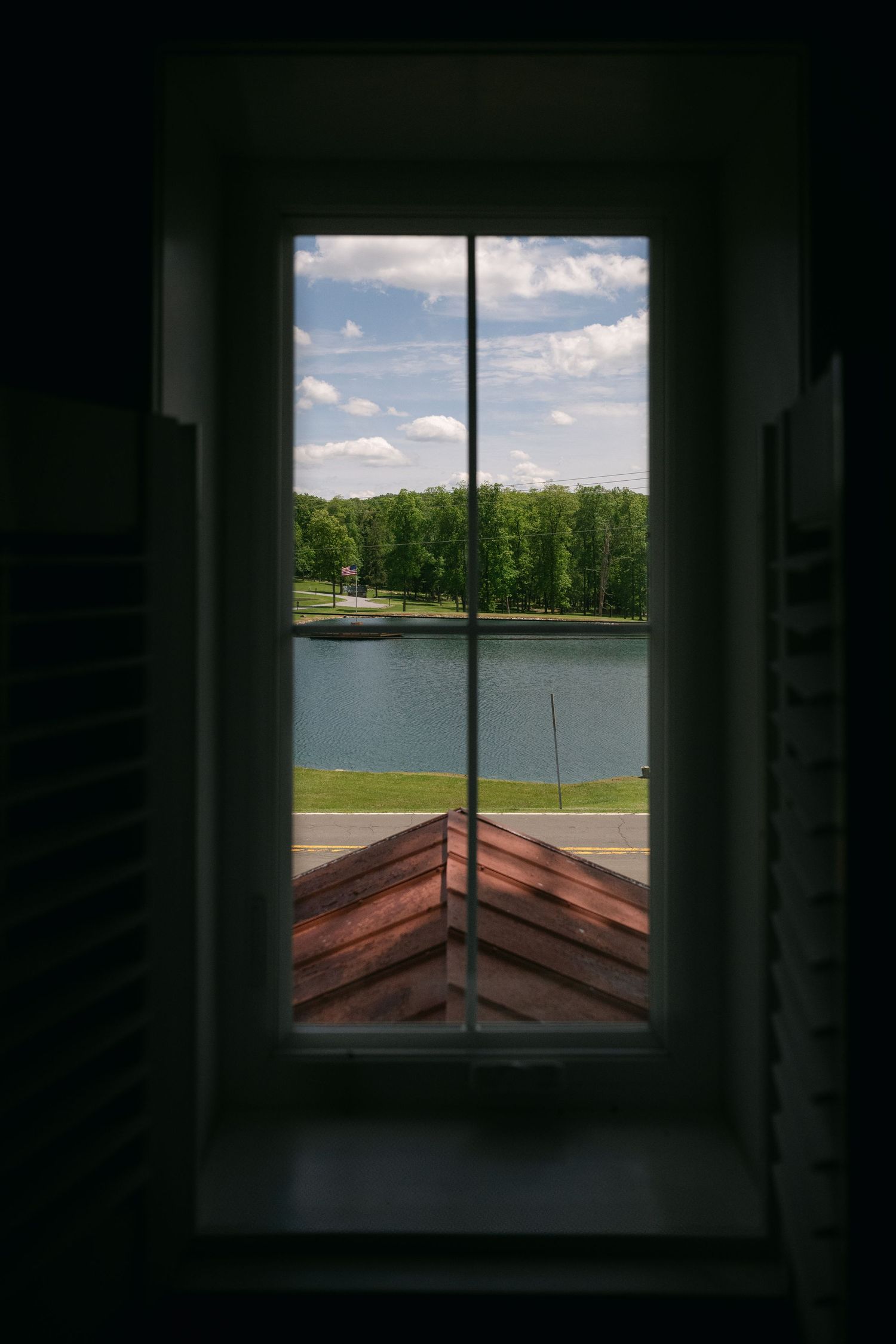 View of a serene lake and trees through a window frame on a sunny day.