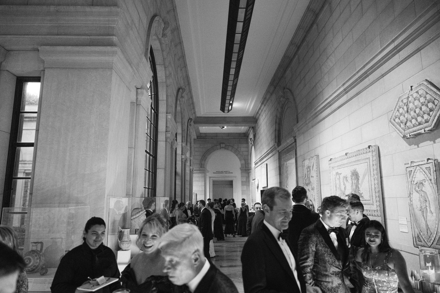Black and white photograph showing guests mingling in an ornate hallway.
