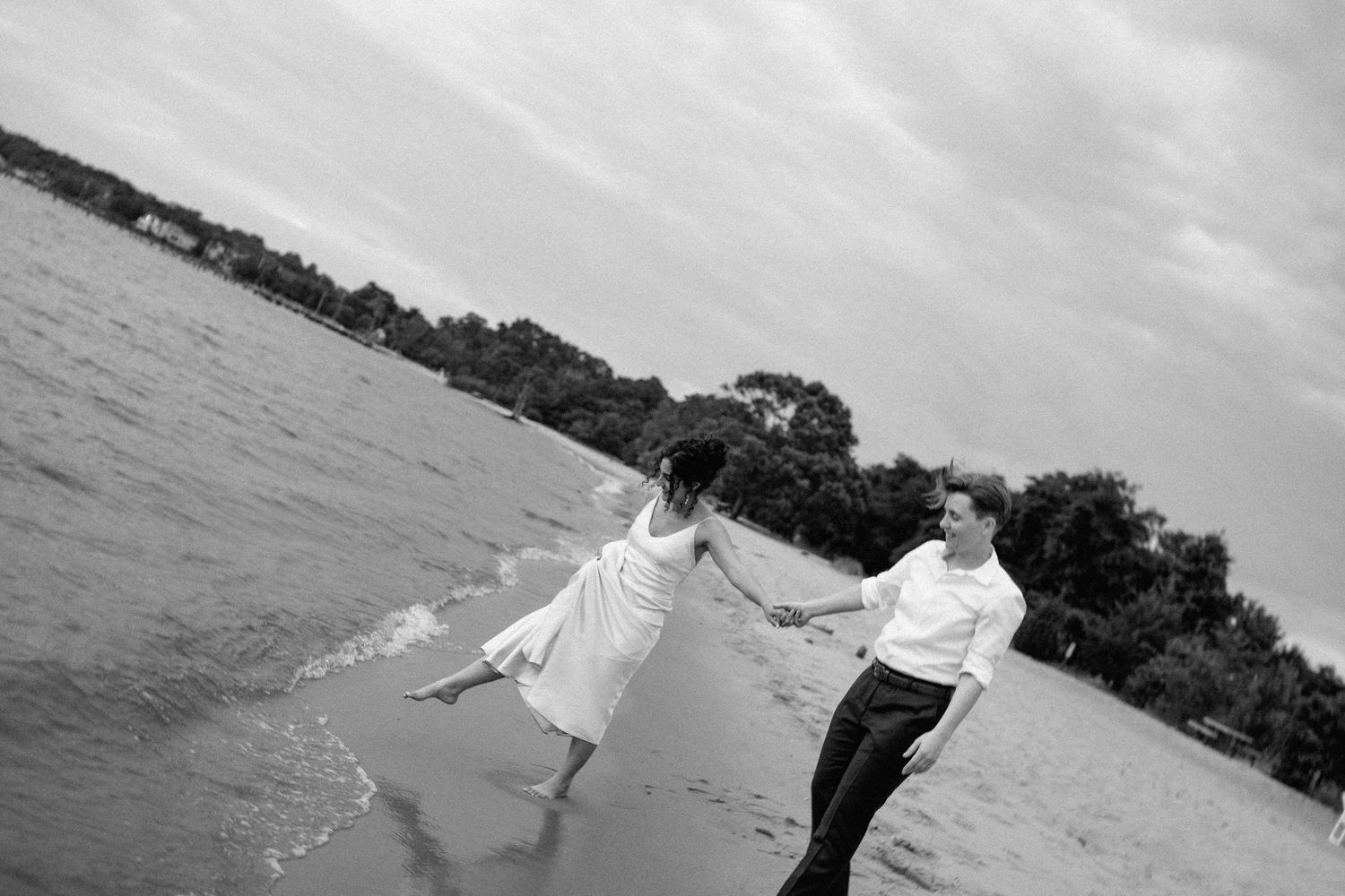 Black and white photo of couple walking along a beach shoreline.
