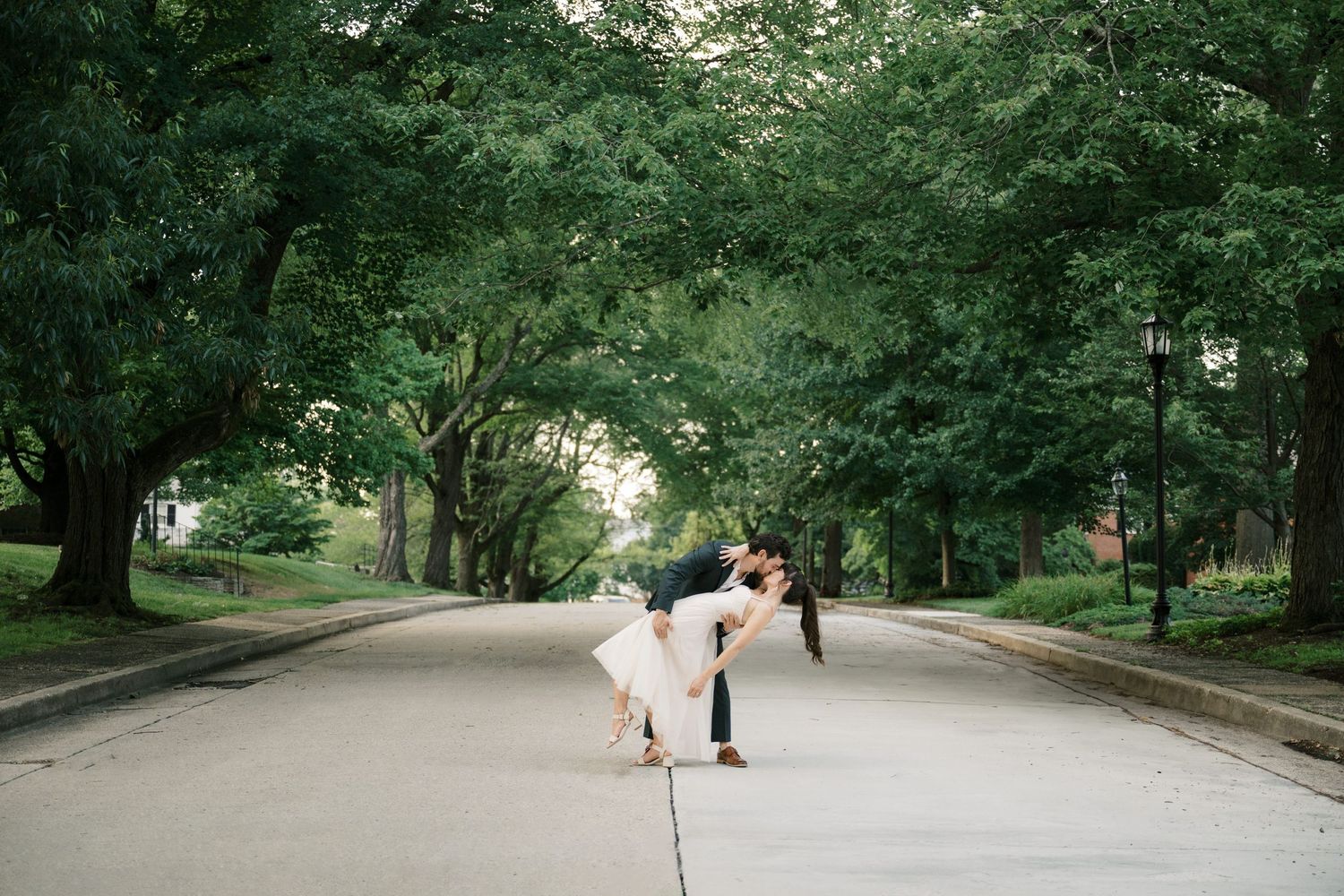 A couple dips romantically on a tree-lined street during a summer photo session.