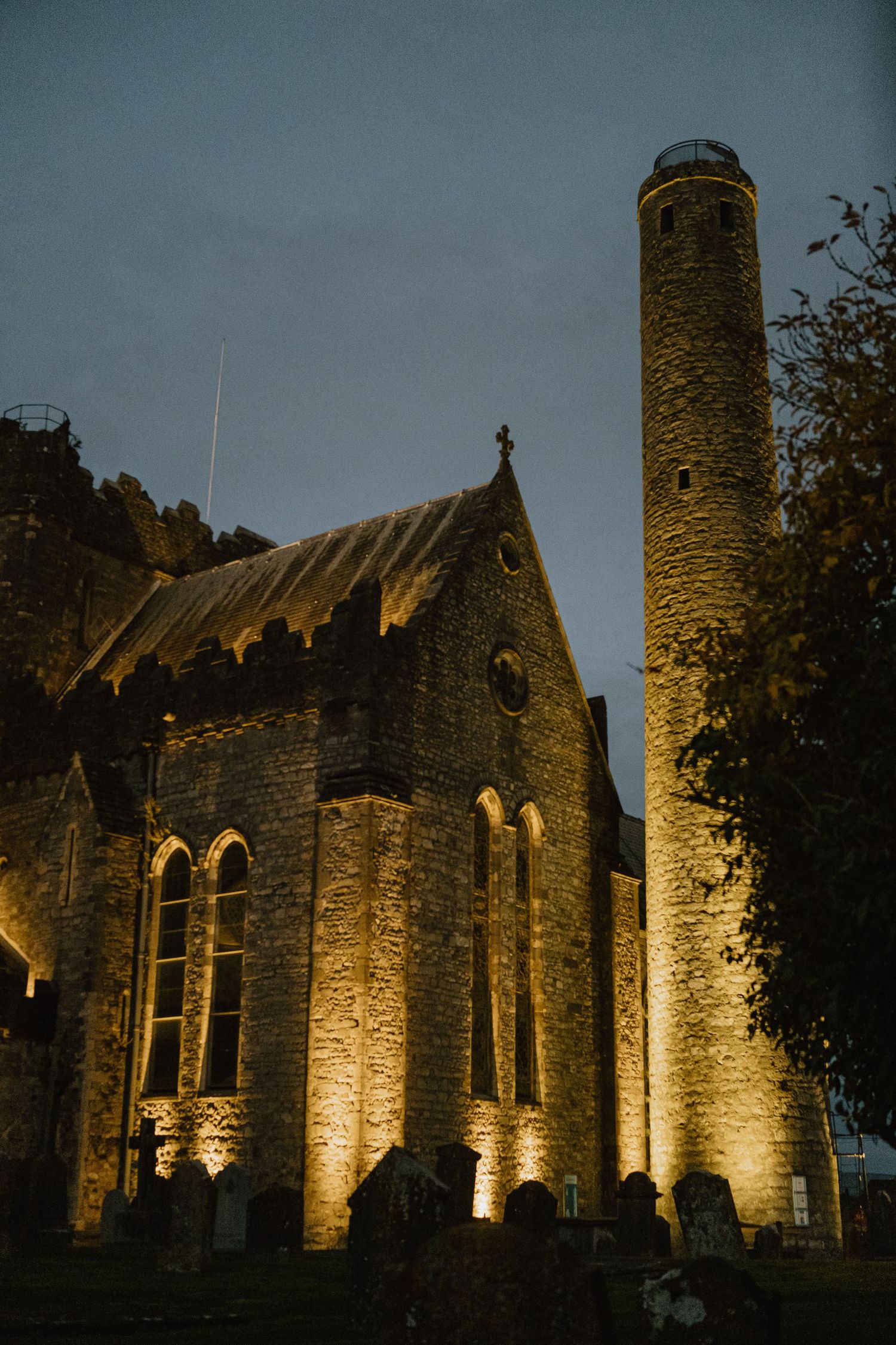 Illuminated stone church and round tower at night with dramatic lighting.