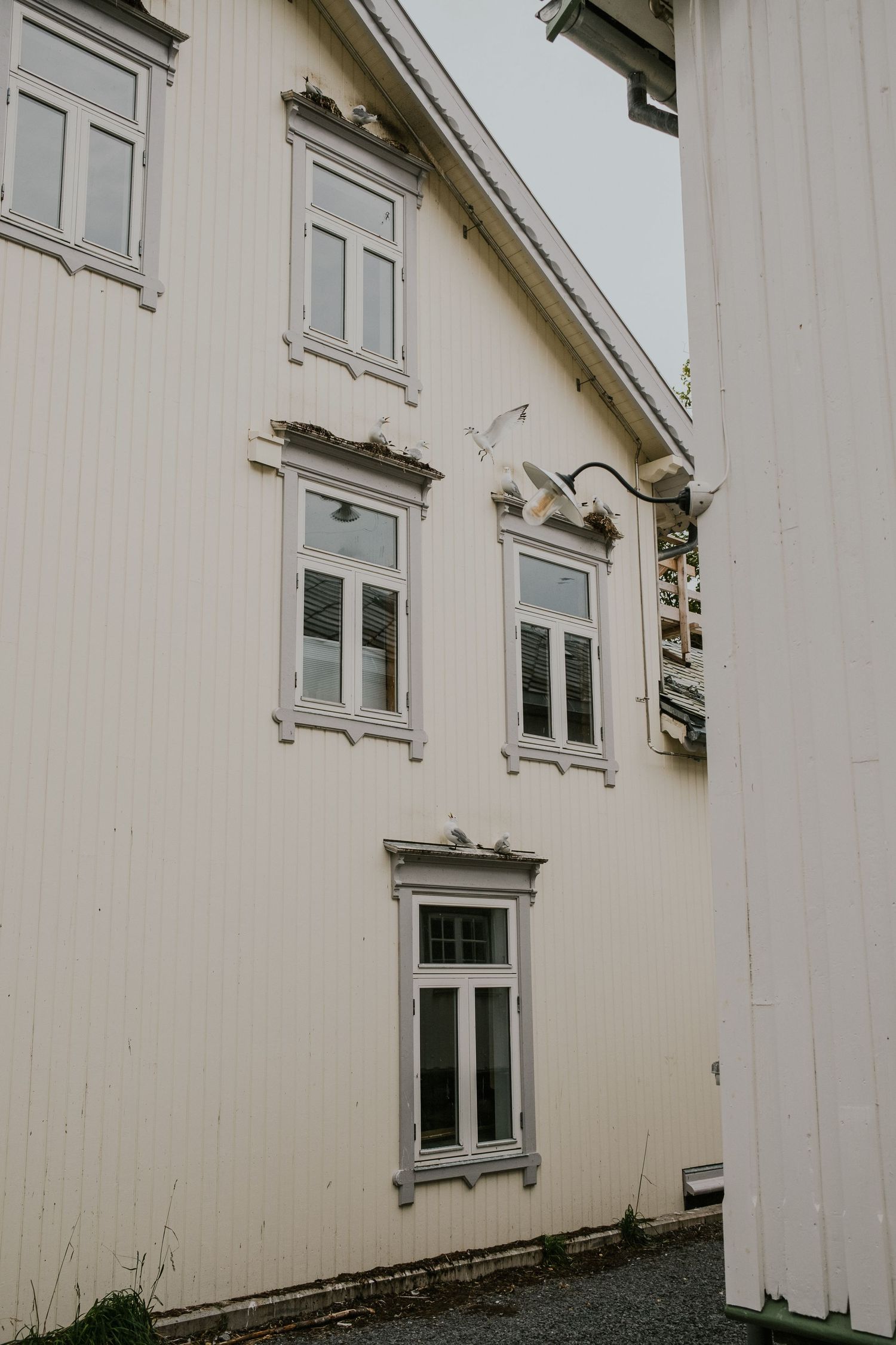 White wooden house with traditional Nordic-style windows and trim details against an overcast sky.