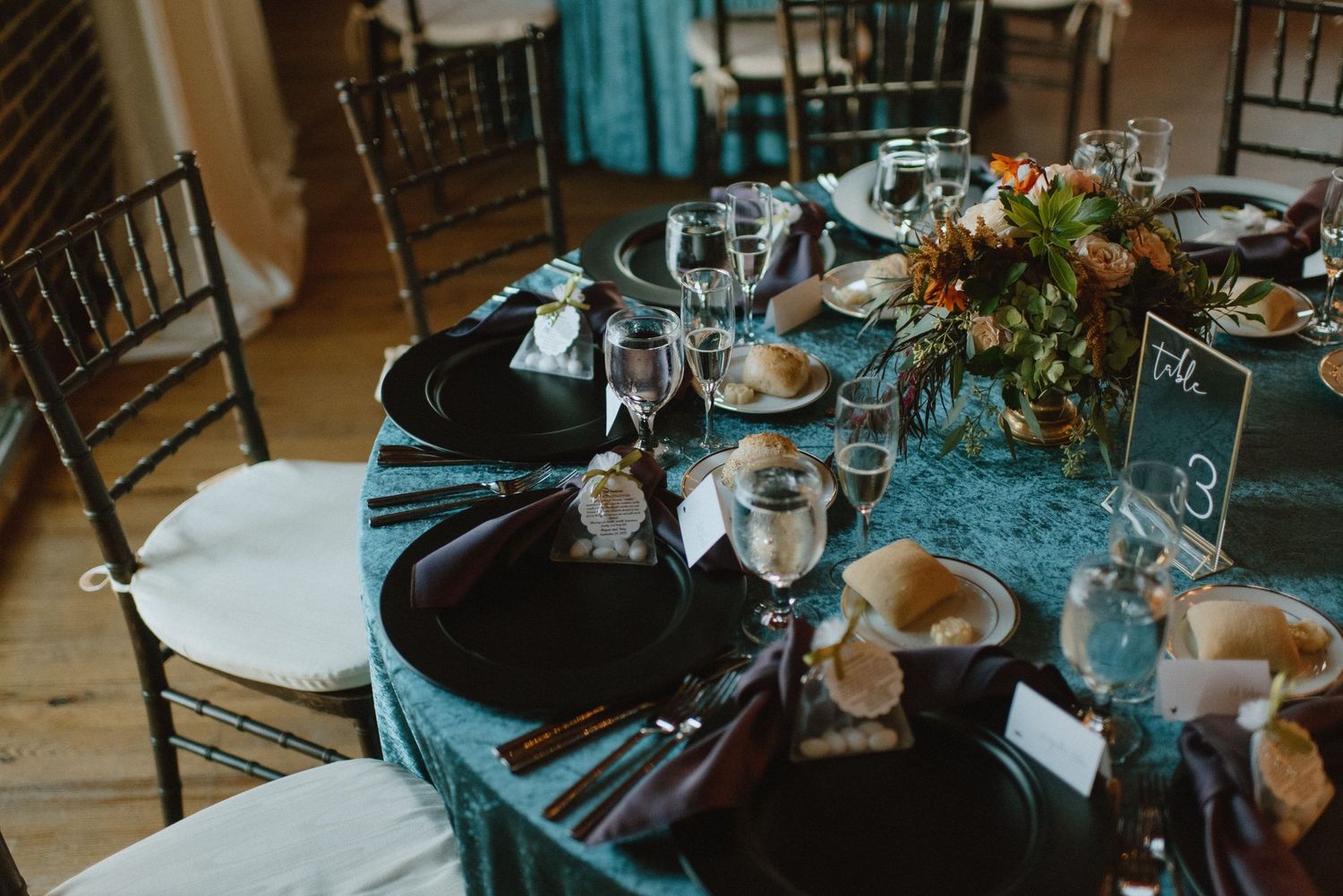 An intimate table setting with teal linens, black plates and elegant floral centerpieces.